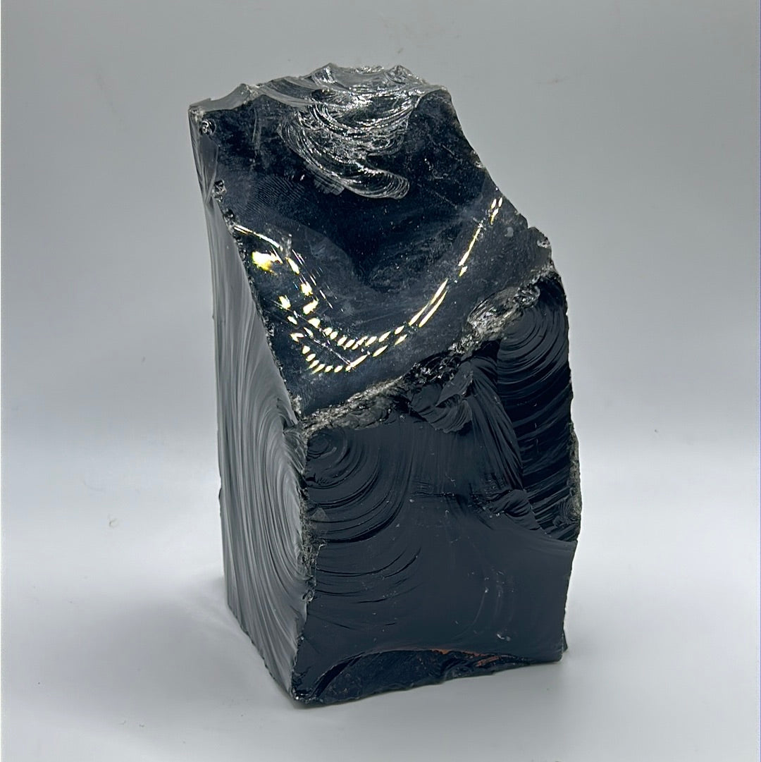 A rough cut freeform piece of Black Obsidian, showcasing its glossy black surface and unique shape, measuring approximately 5.5 inches by 4 inches.