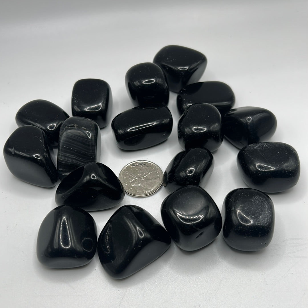 A collection of smooth, shiny Black Obsidian tumbled healing stones, showcasing their natural volcanic glass texture and dark color.