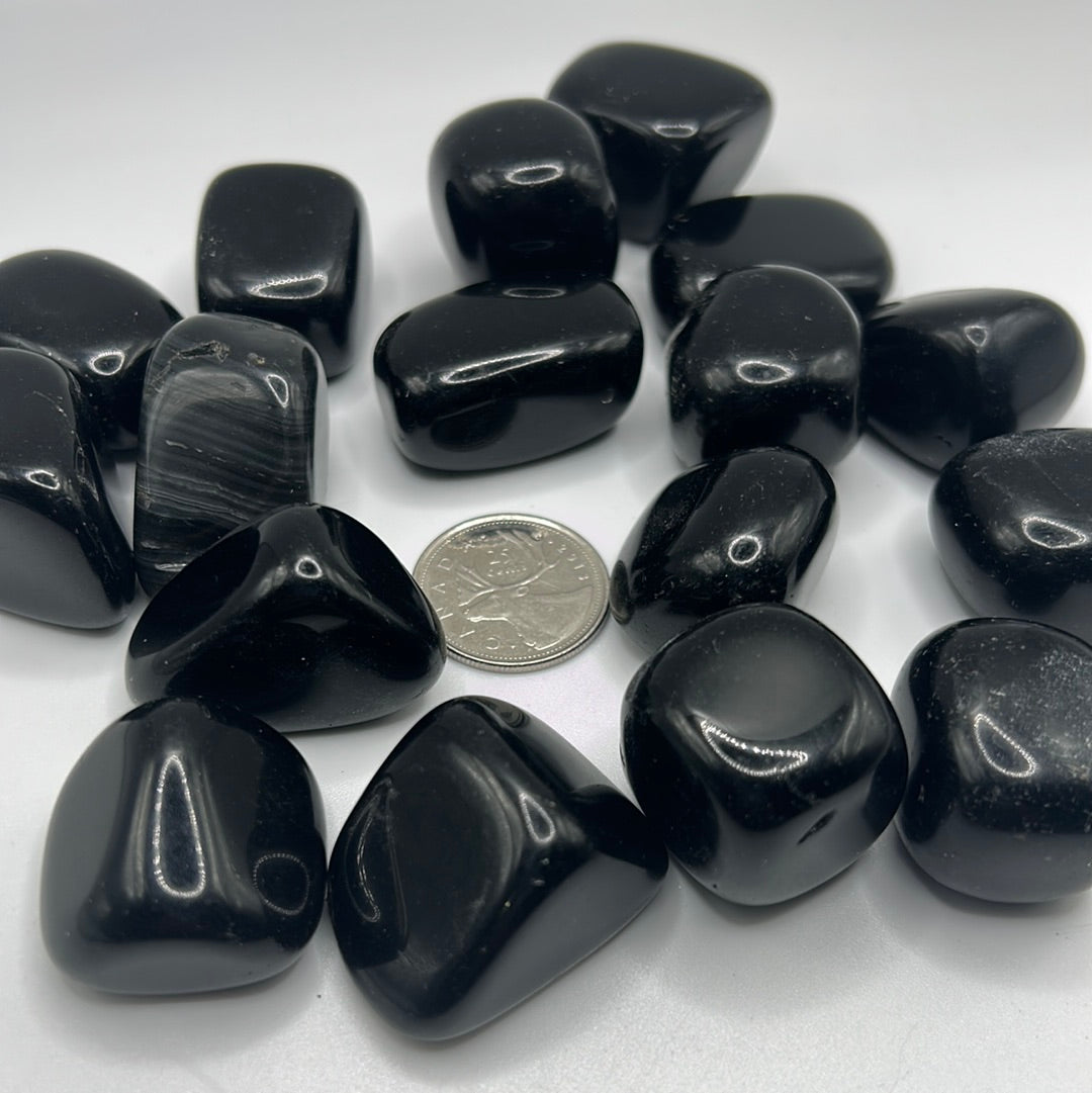 A collection of smooth, shiny Black Obsidian tumbled healing stones, showcasing their natural volcanic glass texture and dark color.