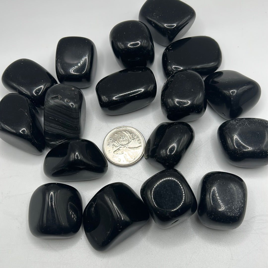 A collection of smooth, shiny Black Obsidian tumbled healing stones, showcasing their natural volcanic glass texture and dark color.