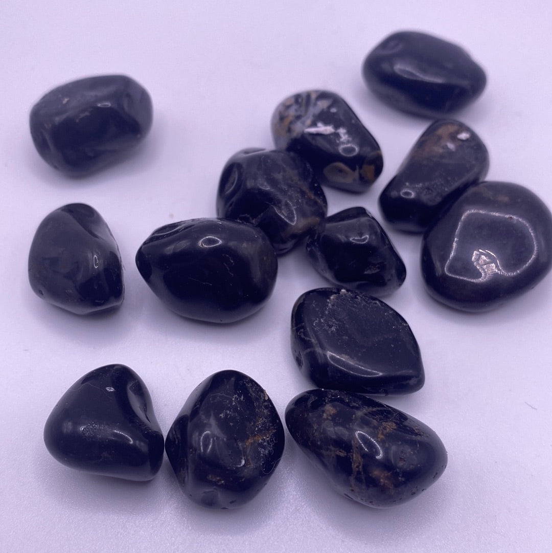 A collection of polished Black Onyx Tumbled Stones in various sizes, showcasing their smooth, glossy surface and deep black color.