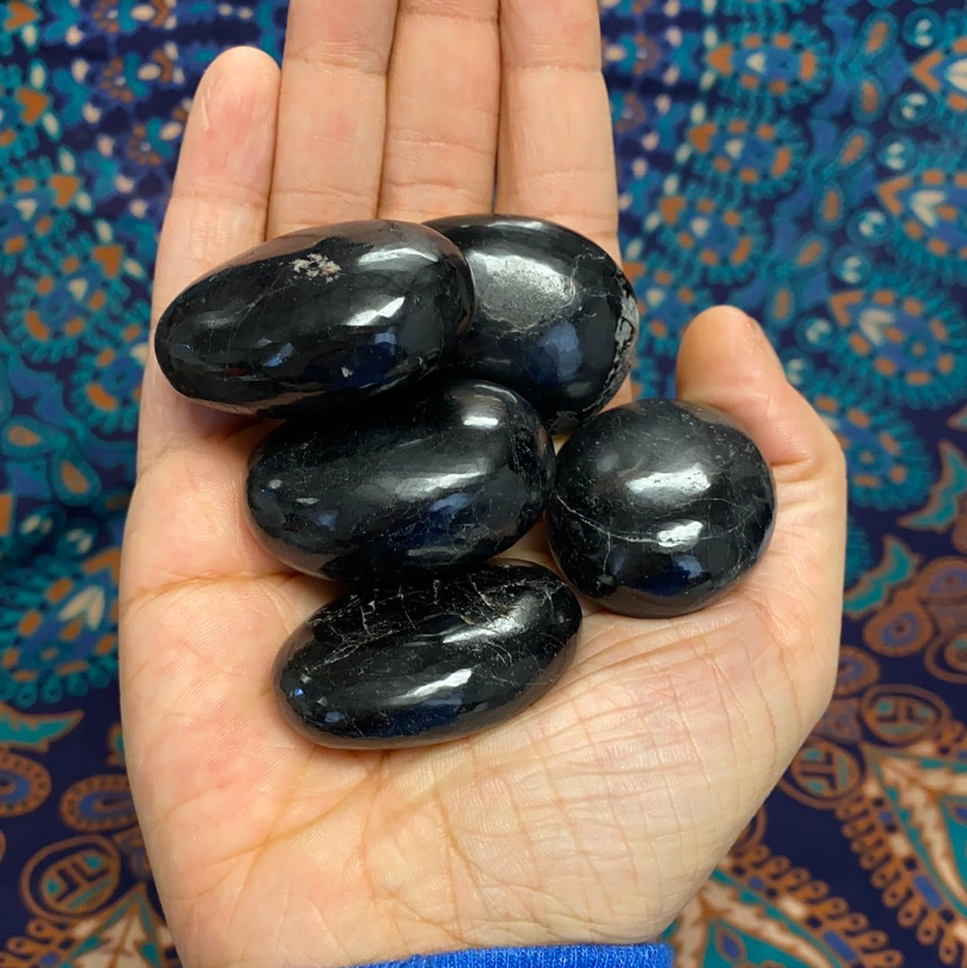 A collection of five unique black tourmaline palm stones, showcasing their natural shapes and textures, perfect for energy protection.