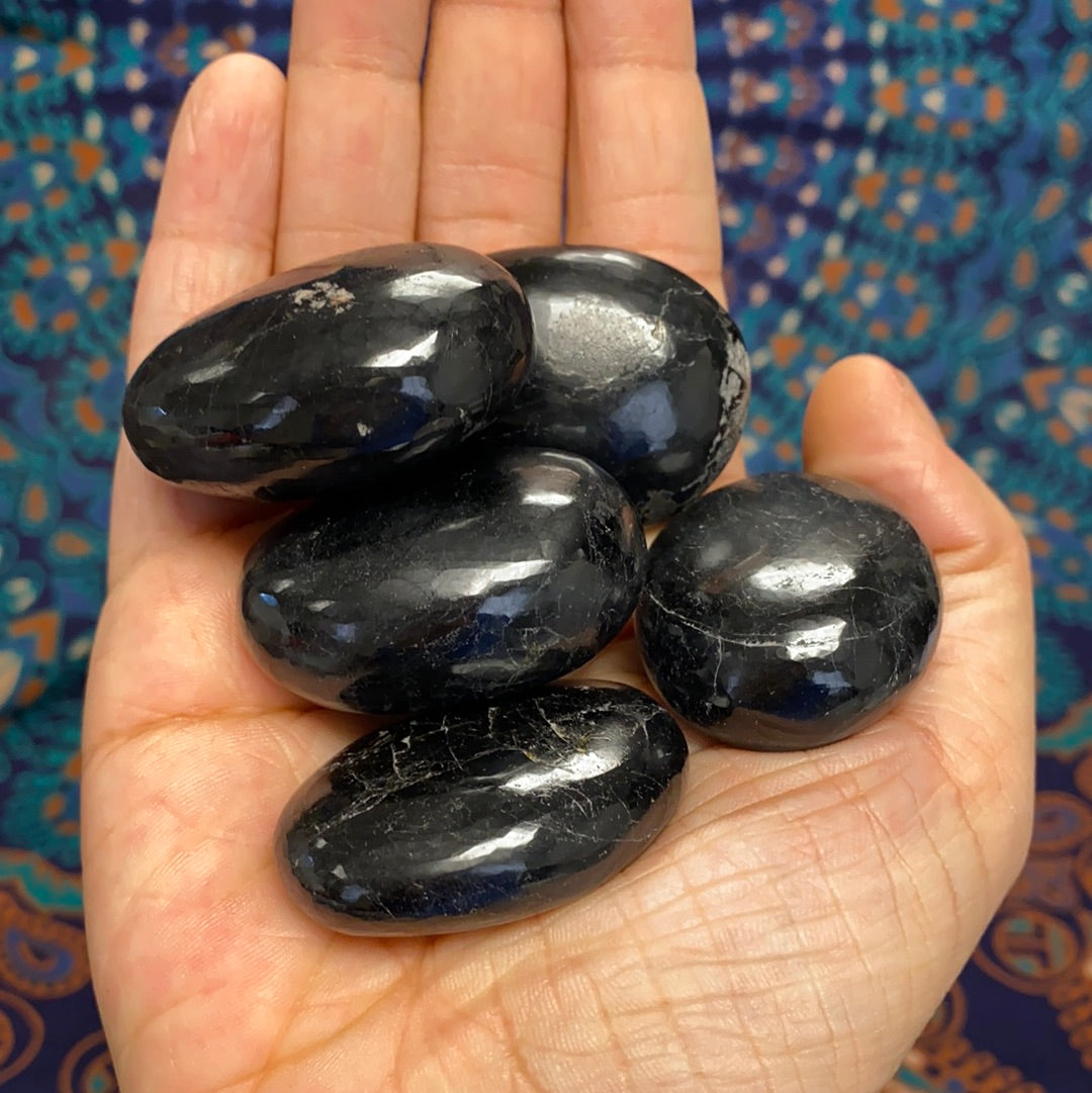 A collection of five unique black tourmaline palm stones, showcasing their natural shapes and textures, perfect for energy protection.