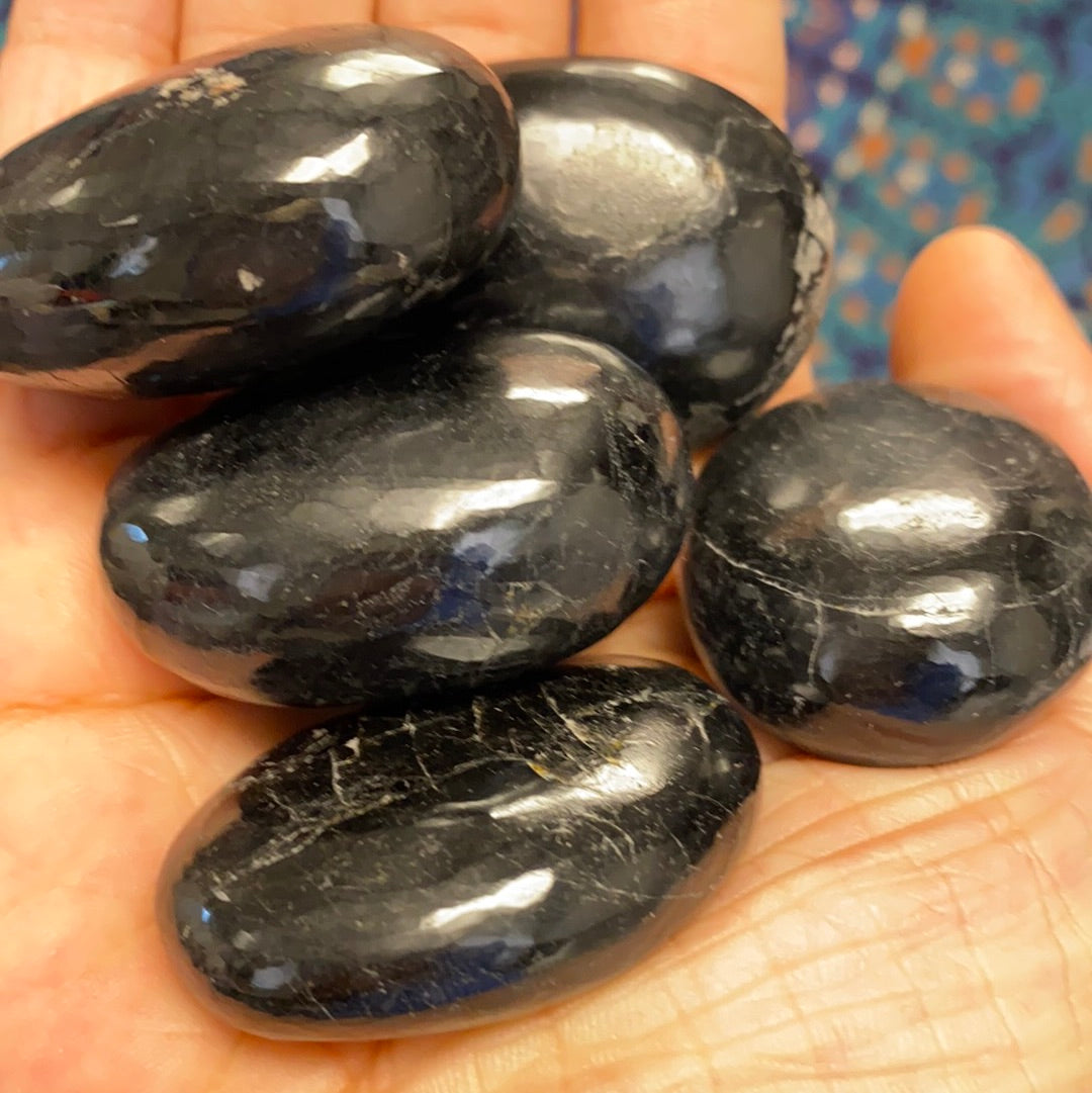 A collection of five unique black tourmaline palm stones, showcasing their natural shapes and textures, perfect for energy protection.