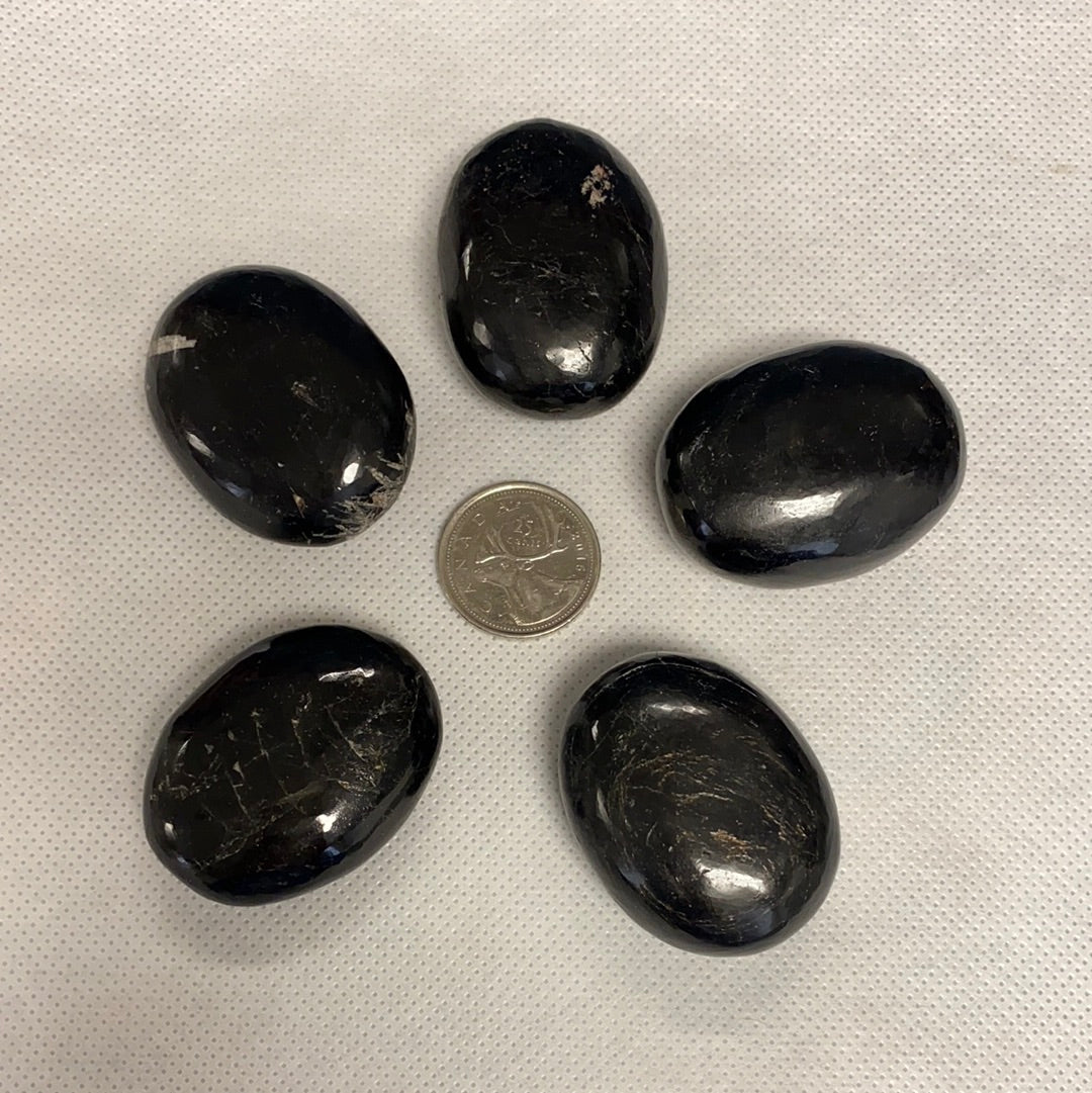 A collection of five unique black tourmaline palm stones, showcasing their natural shapes and textures, perfect for energy protection.