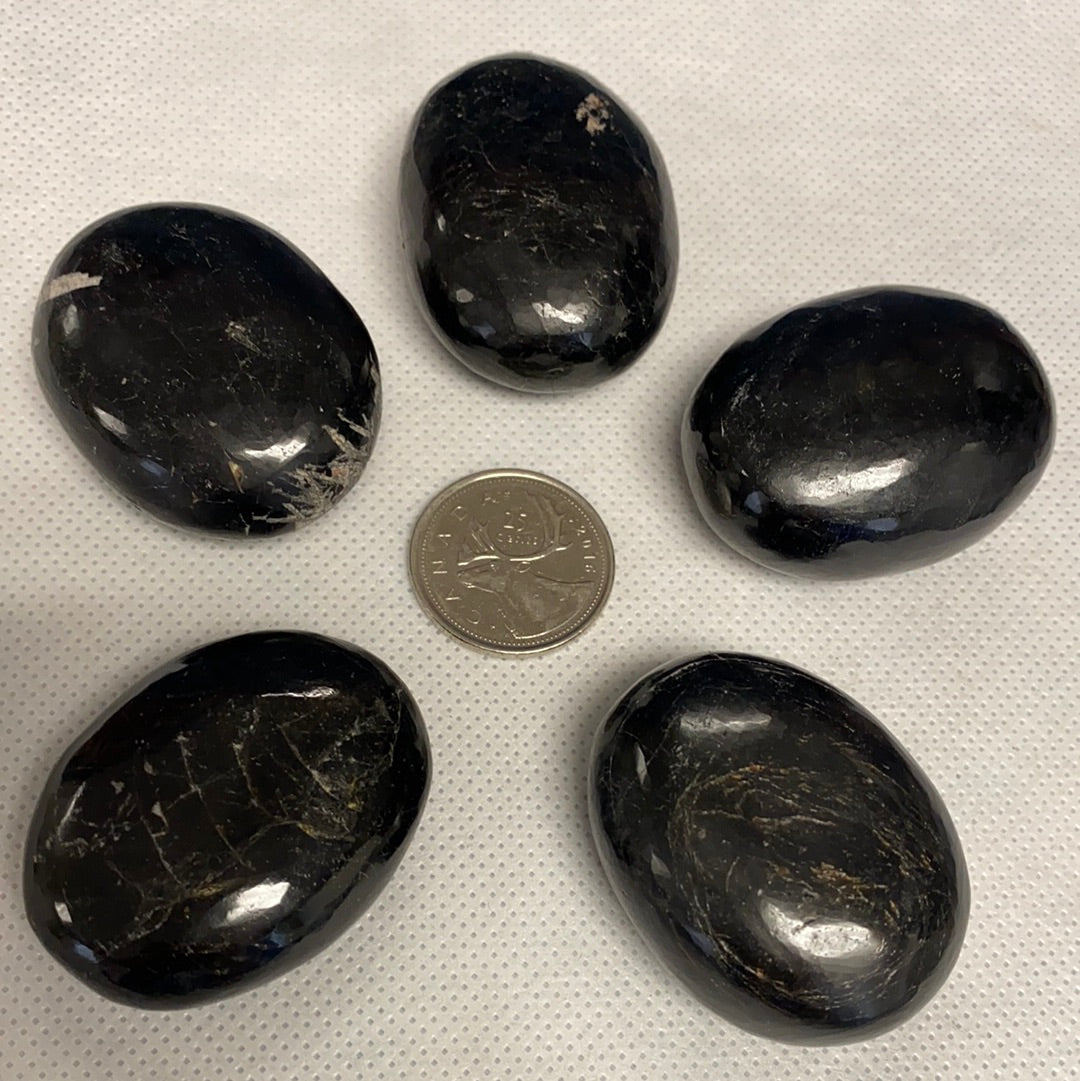 A collection of five unique black tourmaline palm stones, showcasing their natural shapes and textures, perfect for energy protection.