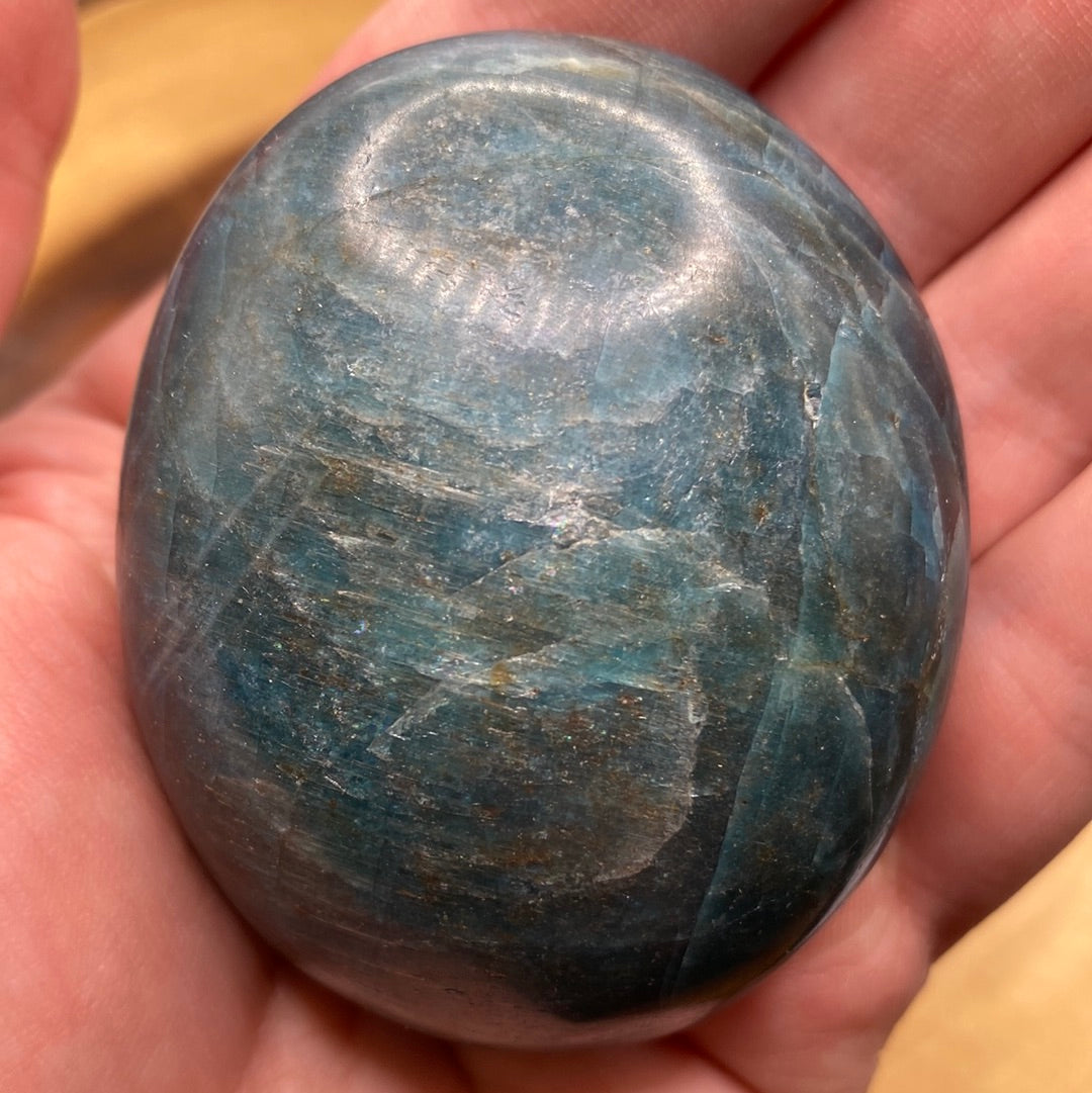 A close-up of a Blue Apatite Palm Stone showcasing its deep blue color with grey and brown speckles, perfect for chakra healing.