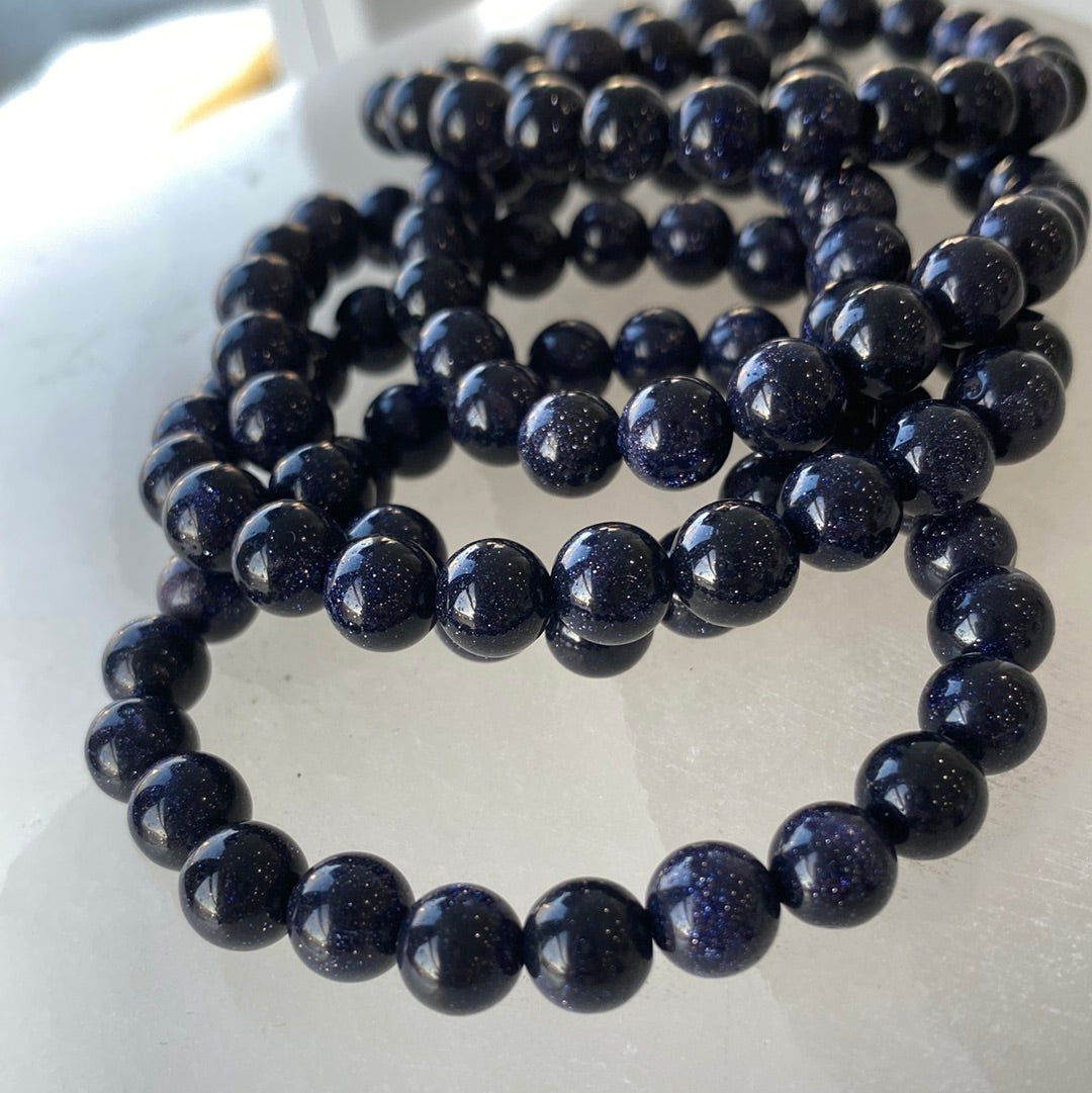 A close-up view of an 8mm Blue Goldstone bracelet showcasing its shimmering blue beads with copper flecks, perfect for metaphysical enthusiasts.