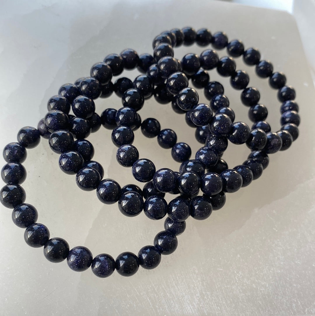 A close-up view of an 8mm Blue Goldstone bracelet showcasing its shimmering blue beads with copper flecks, perfect for metaphysical enthusiasts.