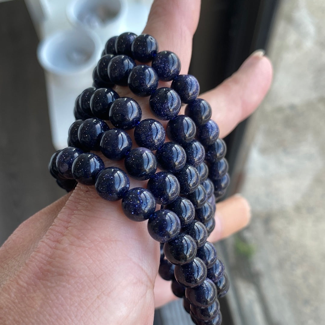 A close-up view of an 8mm Blue Goldstone bracelet showcasing its shimmering blue beads with copper flecks, perfect for metaphysical enthusiasts.