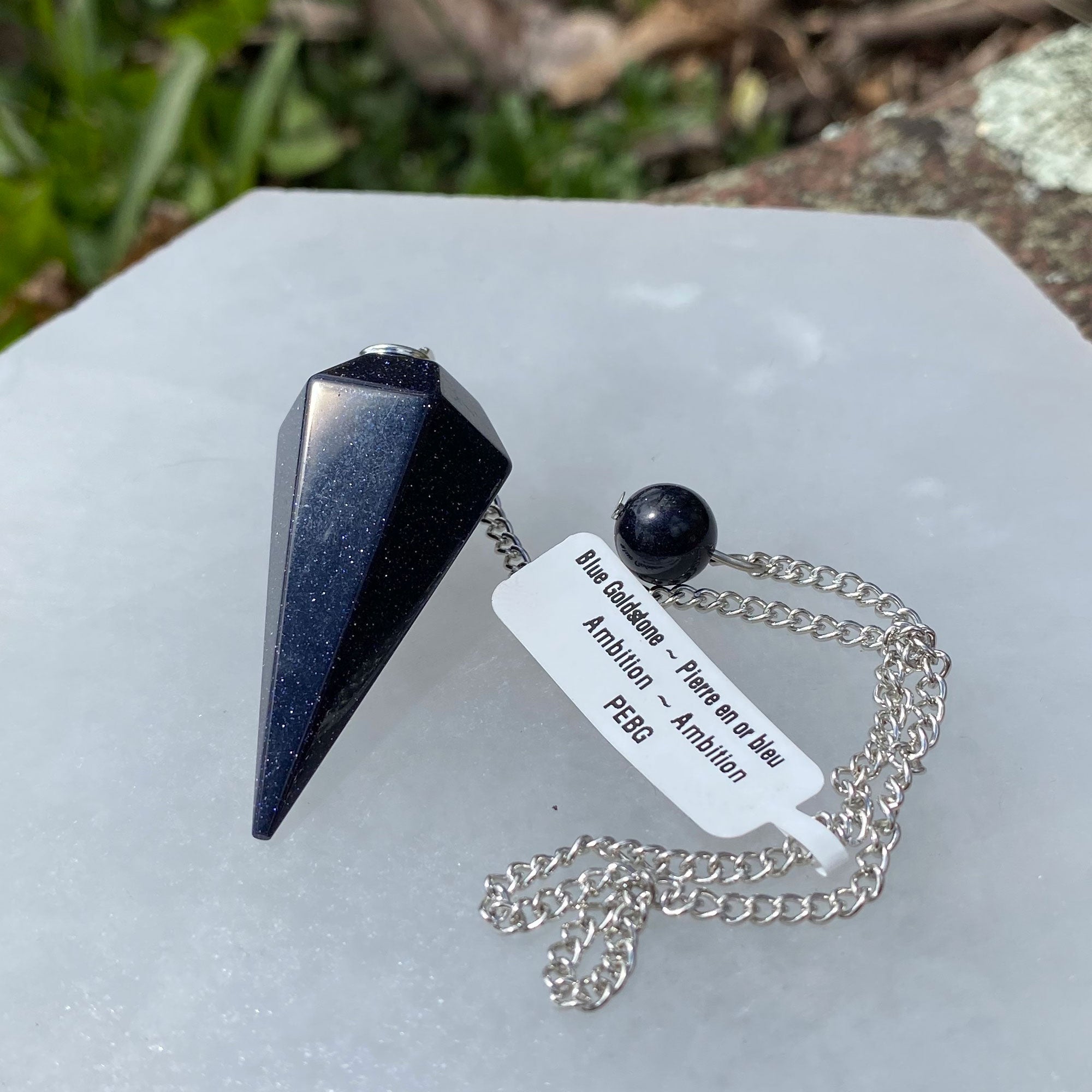 A Blue Goldstone Pendulum on a silver chain, showcasing its shimmering blue and gold flecks, perfect for spiritual guidance and energy work.