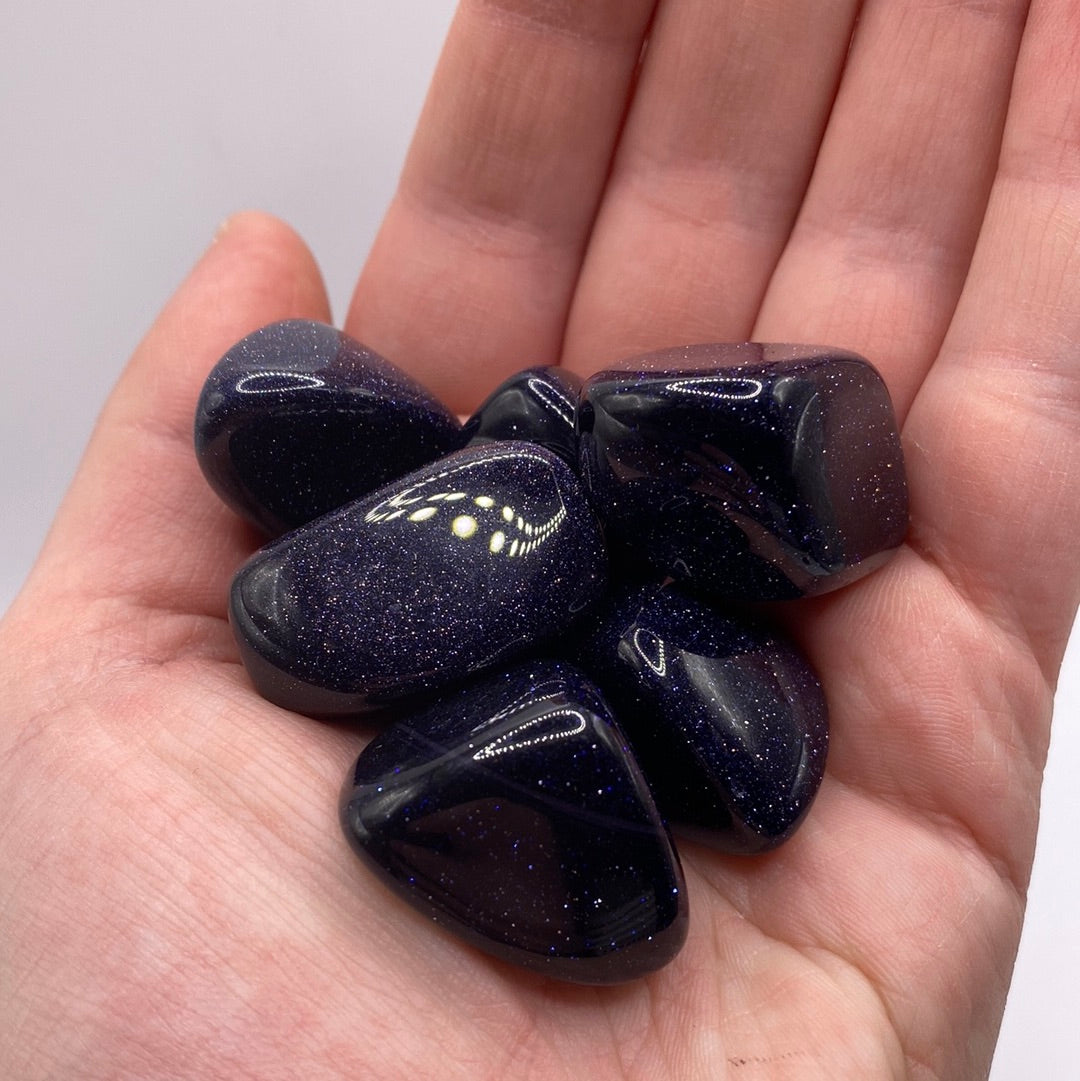 A close-up view of a Blue Goldstone Tumbled crystal showcasing its reflective blue and black speckled surface, radiating positive energy.