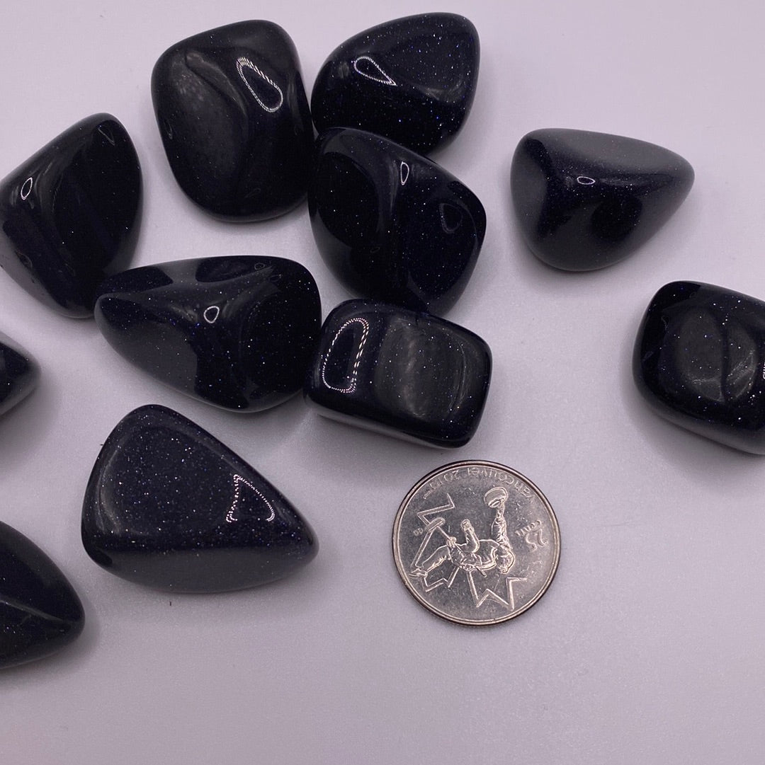 A close-up view of a Blue Goldstone Tumbled crystal showcasing its reflective blue and black speckled surface, radiating positive energy.