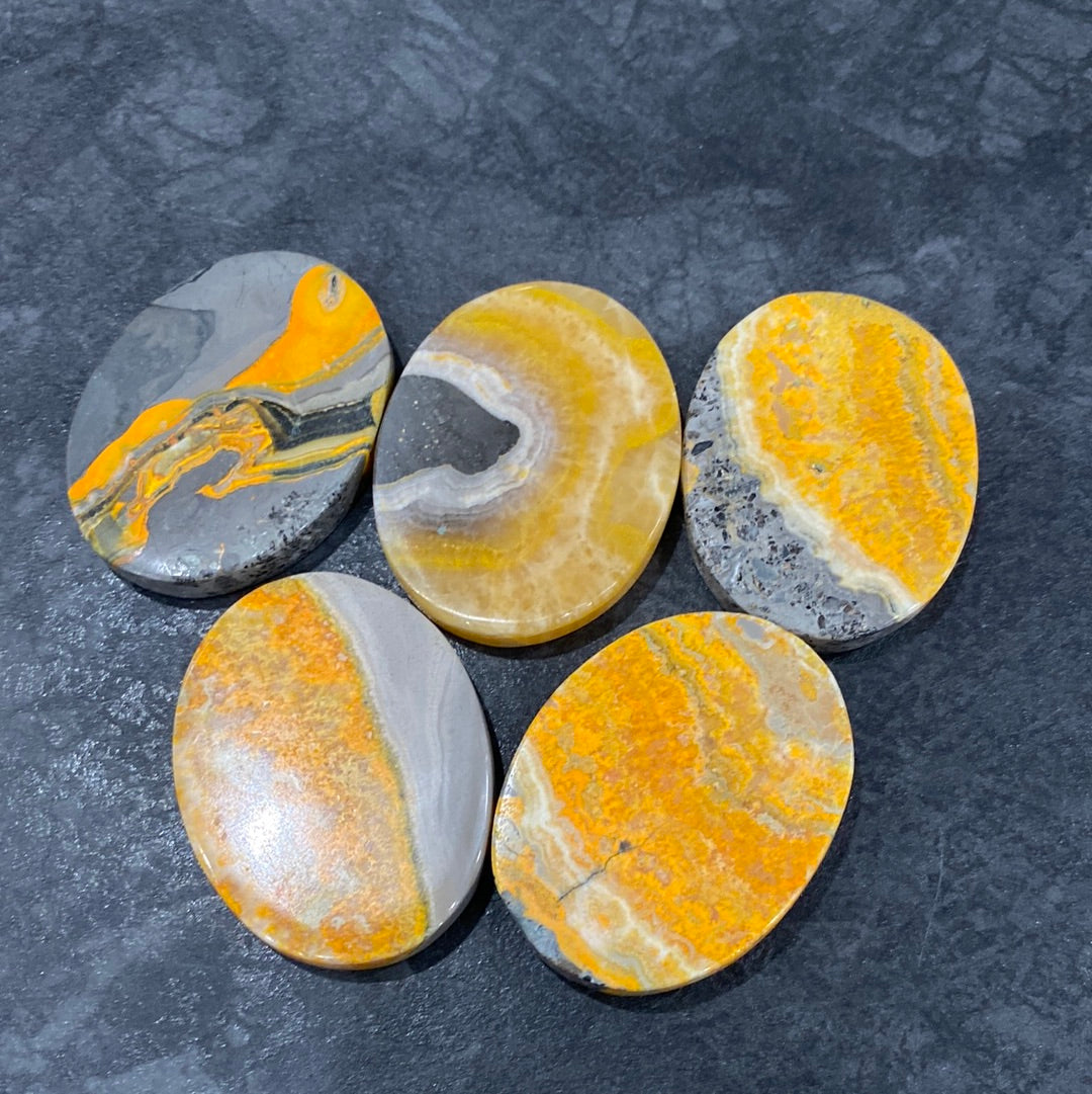 A collection of polished Bumble Bee Jasper ovals, showcasing vibrant yellow, black, and orange patterns, measuring approximately 1.6 inches long.