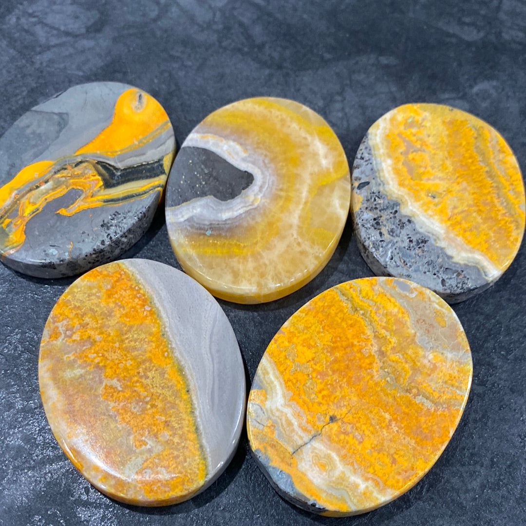 A collection of polished Bumble Bee Jasper ovals, showcasing vibrant yellow, black, and orange patterns, measuring approximately 1.6 inches long.