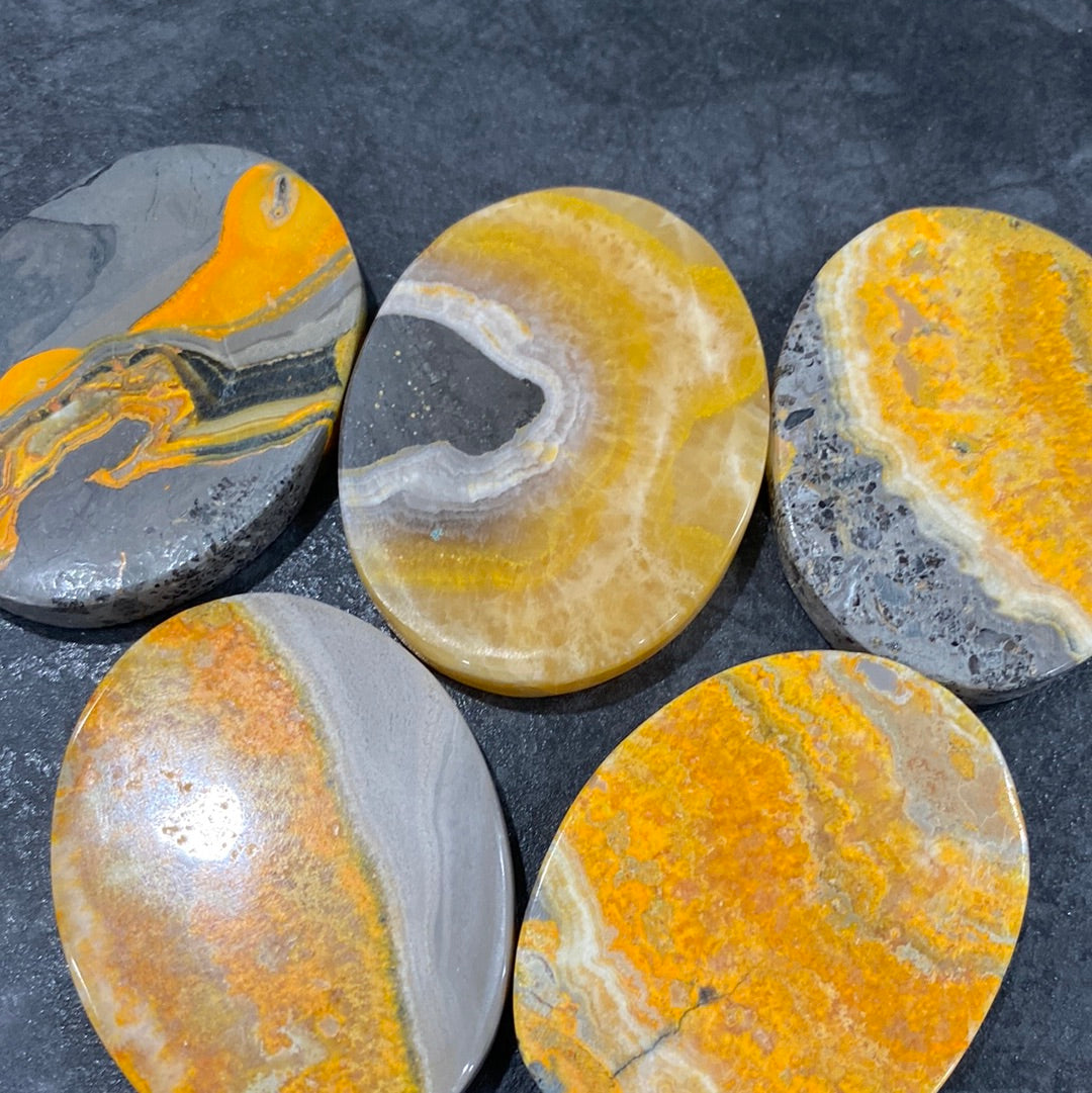 A collection of polished Bumble Bee Jasper ovals, showcasing vibrant yellow, black, and orange patterns, measuring approximately 1.6 inches long.