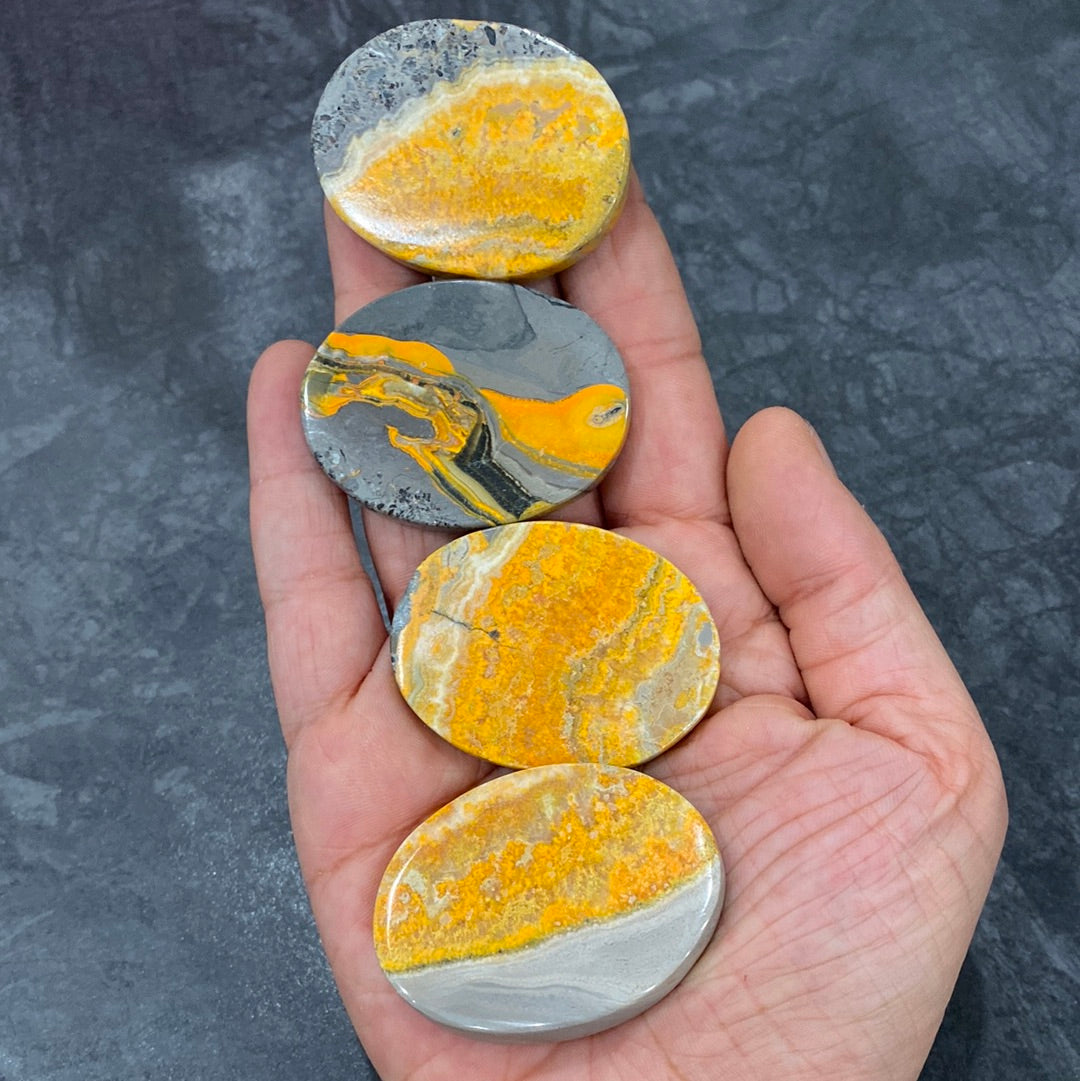 A collection of polished Bumble Bee Jasper ovals, showcasing vibrant yellow, black, and orange patterns, measuring approximately 1.6 inches long.