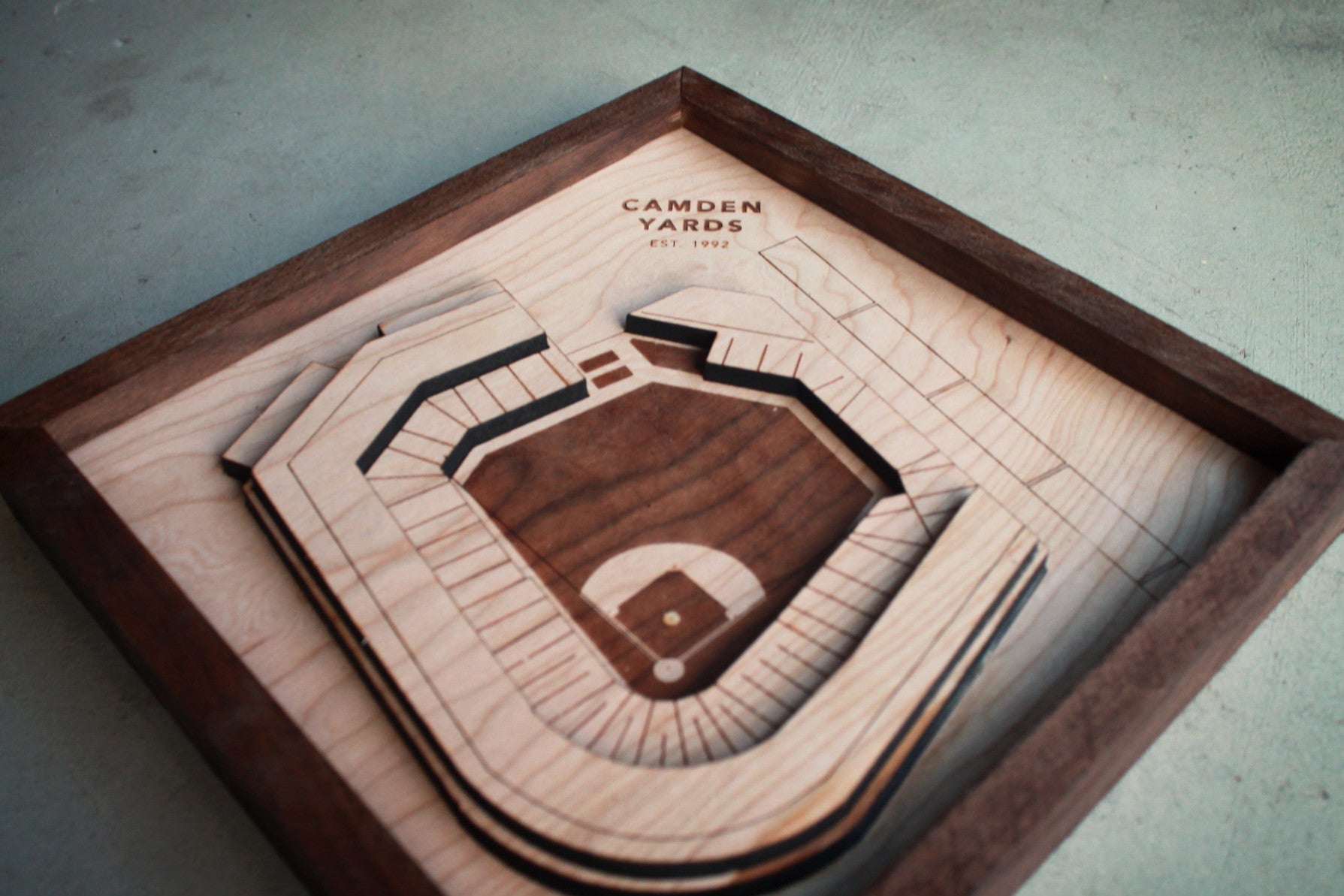 A detailed wooden replica of Camden Yards stadium, showcasing premium hardwood craftsmanship with a black walnut frame.