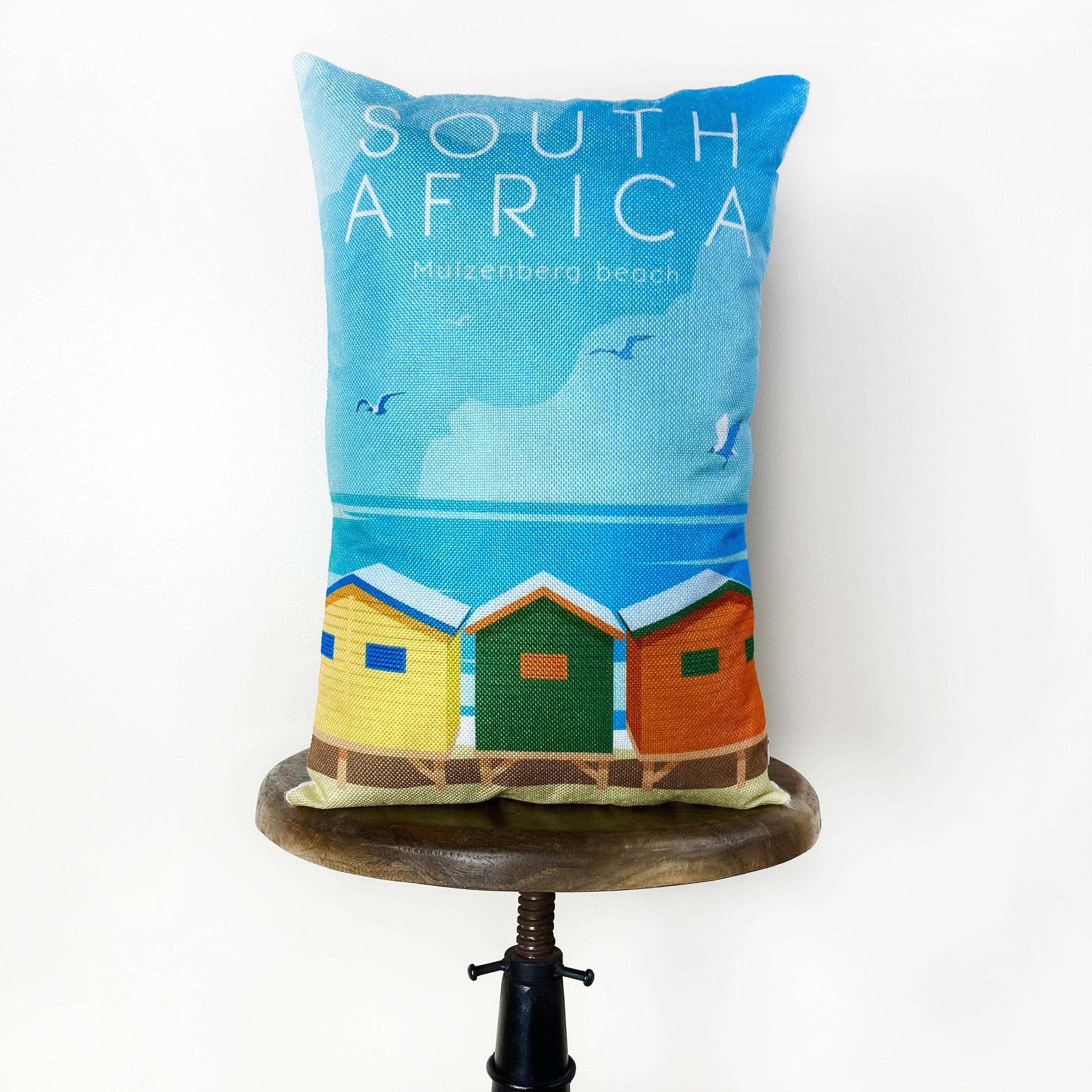 Handmade 12x18 pillow cover featuring a colorful travel poster of Muizenberg Beach in Cape Town, South Africa.