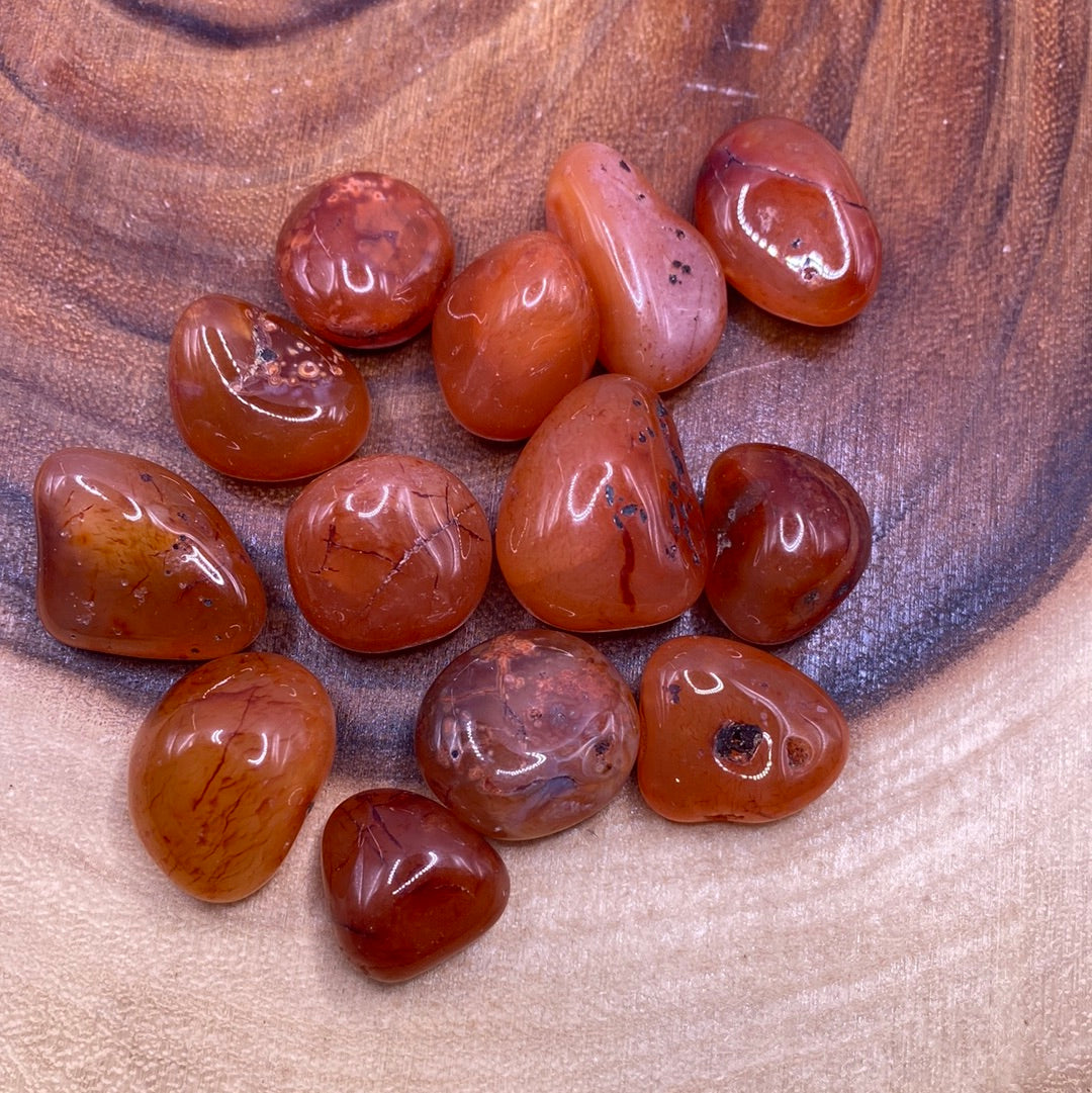 A close-up of a Carnelian Tumbled (M) crystal showcasing its reddish-orange color and unique banded patterns.