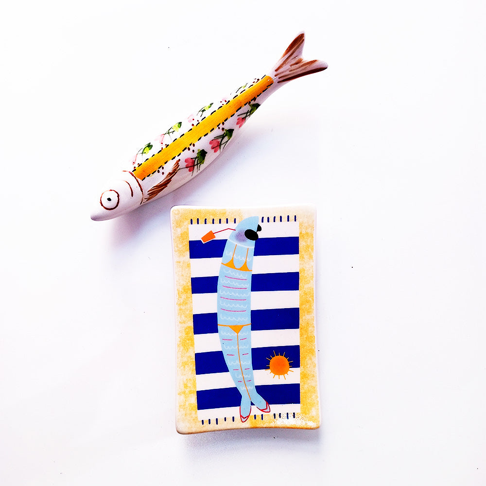 A whimsical ceramic soap dish featuring a hand-painted sardine enjoying a sunny day at the beach, perfect for adding charm to your bathroom.