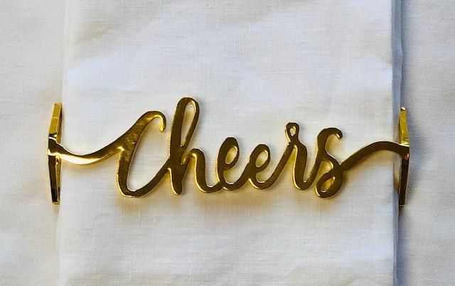 Set of 4 shiny gold napkin wraps with 'cheers' design, elegantly displayed on a dining table.