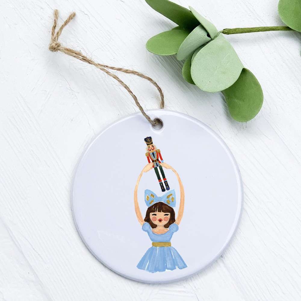 Clara Holding Nutcracker porcelain ornament with a glossy finish, featuring a colorful design, measuring 2.75 inches in diameter.