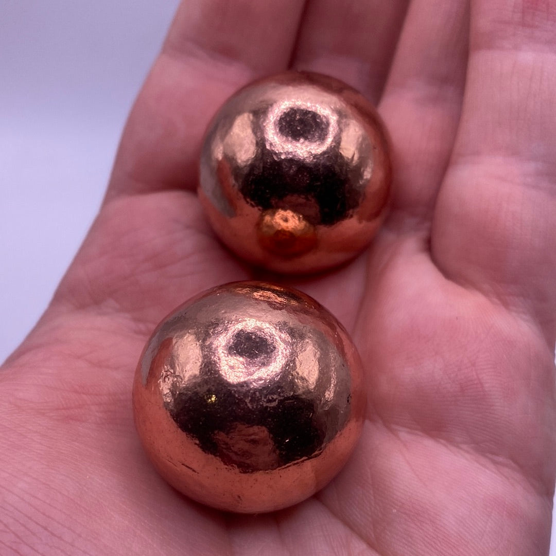 A polished red-orange Copper Ball resting in a velvet pouch, showcasing its shine and clarity.