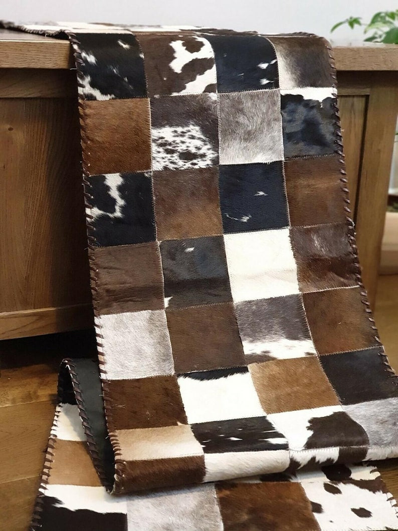 A stylish 16" x 96" cow skin table runner featuring a contemporary square pattern, showcasing its genuine leather texture and colors.