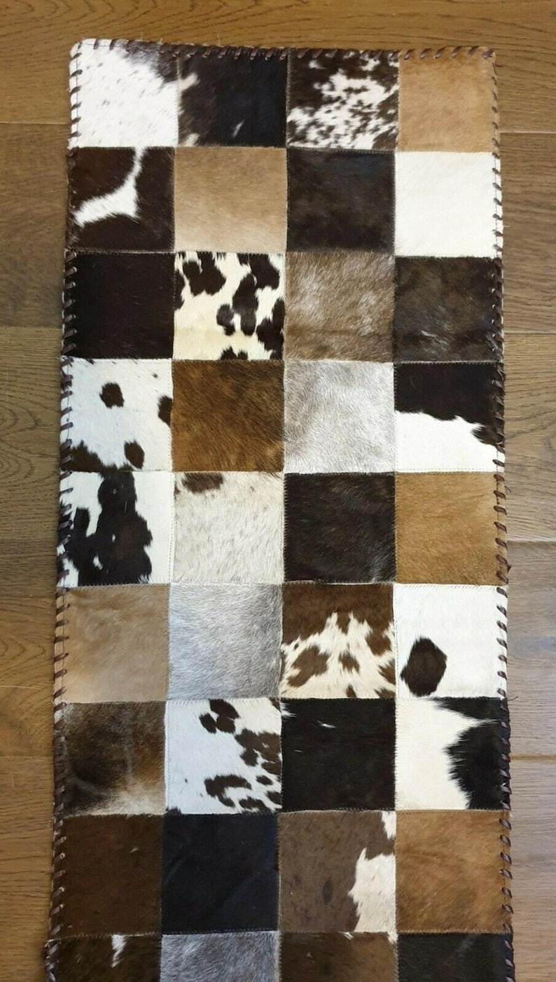 A stylish 16" x 96" cow skin table runner featuring a contemporary square pattern, showcasing its genuine leather texture and colors.