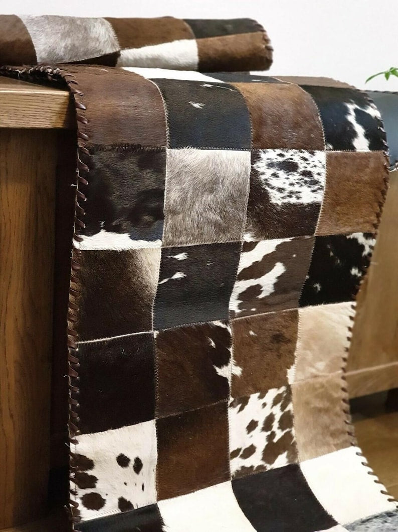 A stylish 16" x 96" cow skin table runner featuring a contemporary square pattern, showcasing its genuine leather texture and colors.