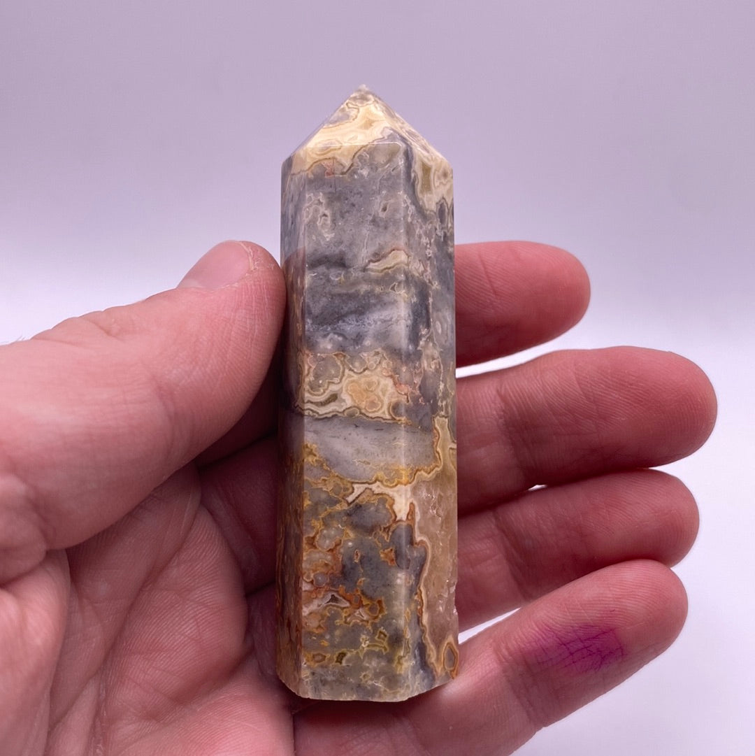 A polished point of Crazy Lace Agate showcasing intricate red and white lace patterns with hints of grey and yellow.