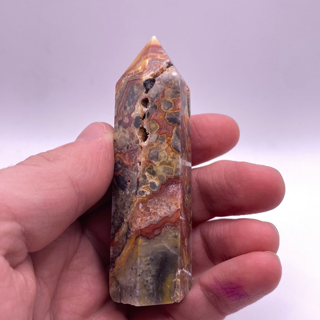 A polished point of Crazy Lace Agate showcasing intricate red and white lace patterns with hints of grey and yellow.