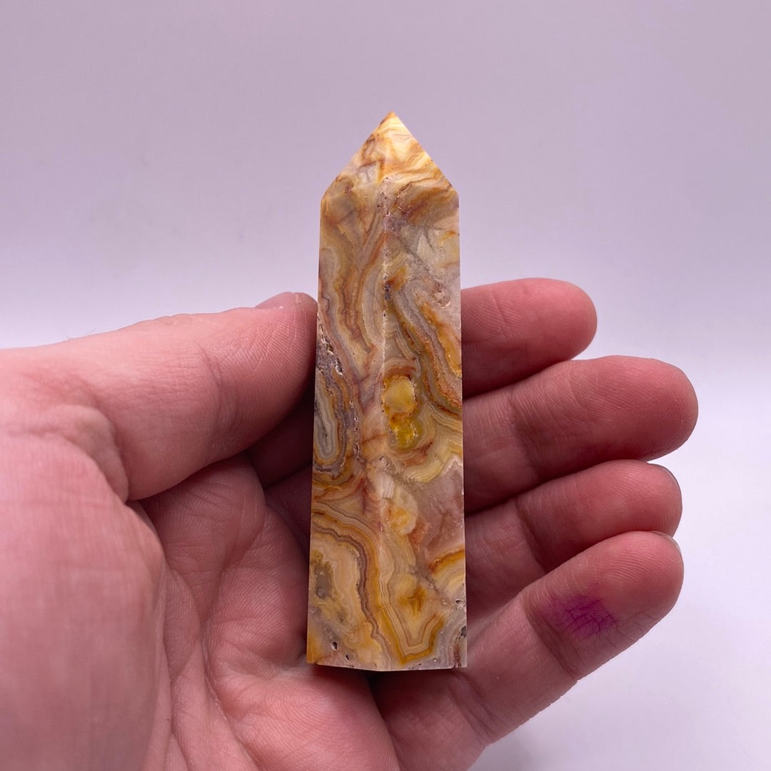 A polished point of Crazy Lace Agate showcasing intricate red and white lace patterns with hints of grey and yellow.