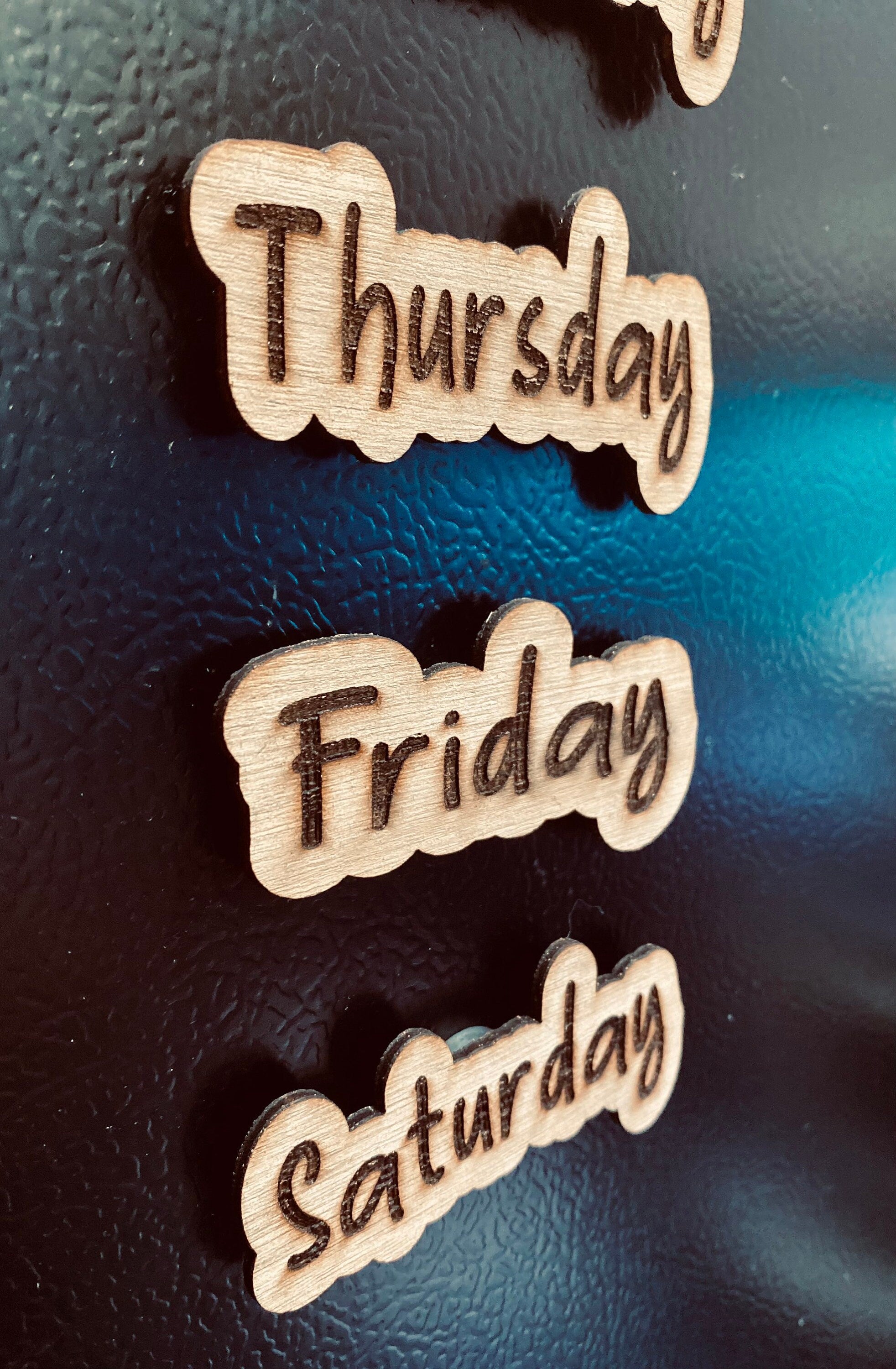 Set of wooden Days of the Week Magnets displayed on a fridge, showcasing their natural finish and laser engraved design.