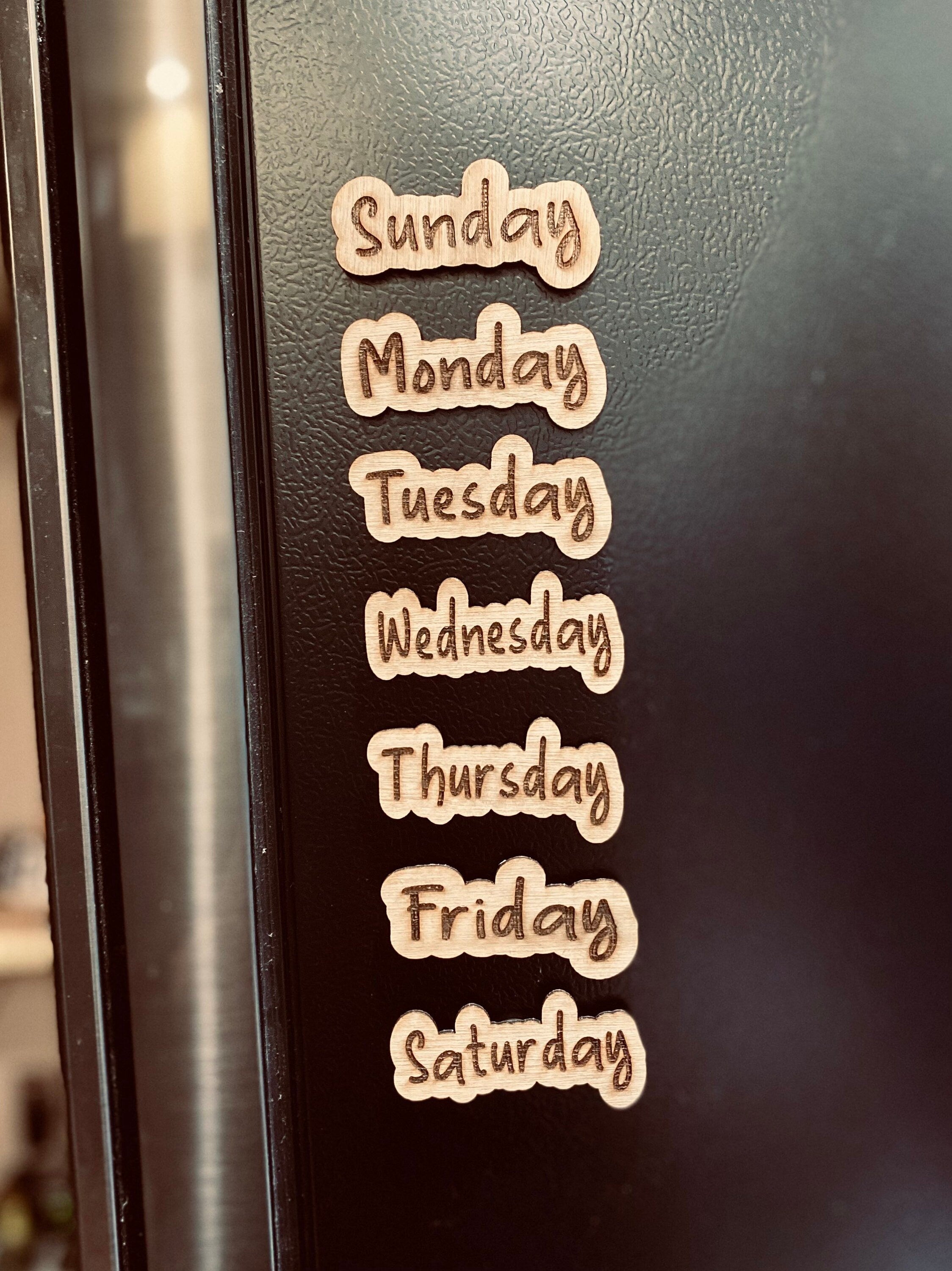 Set of wooden Days of the Week Magnets displayed on a fridge, showcasing their natural finish and laser engraved design.