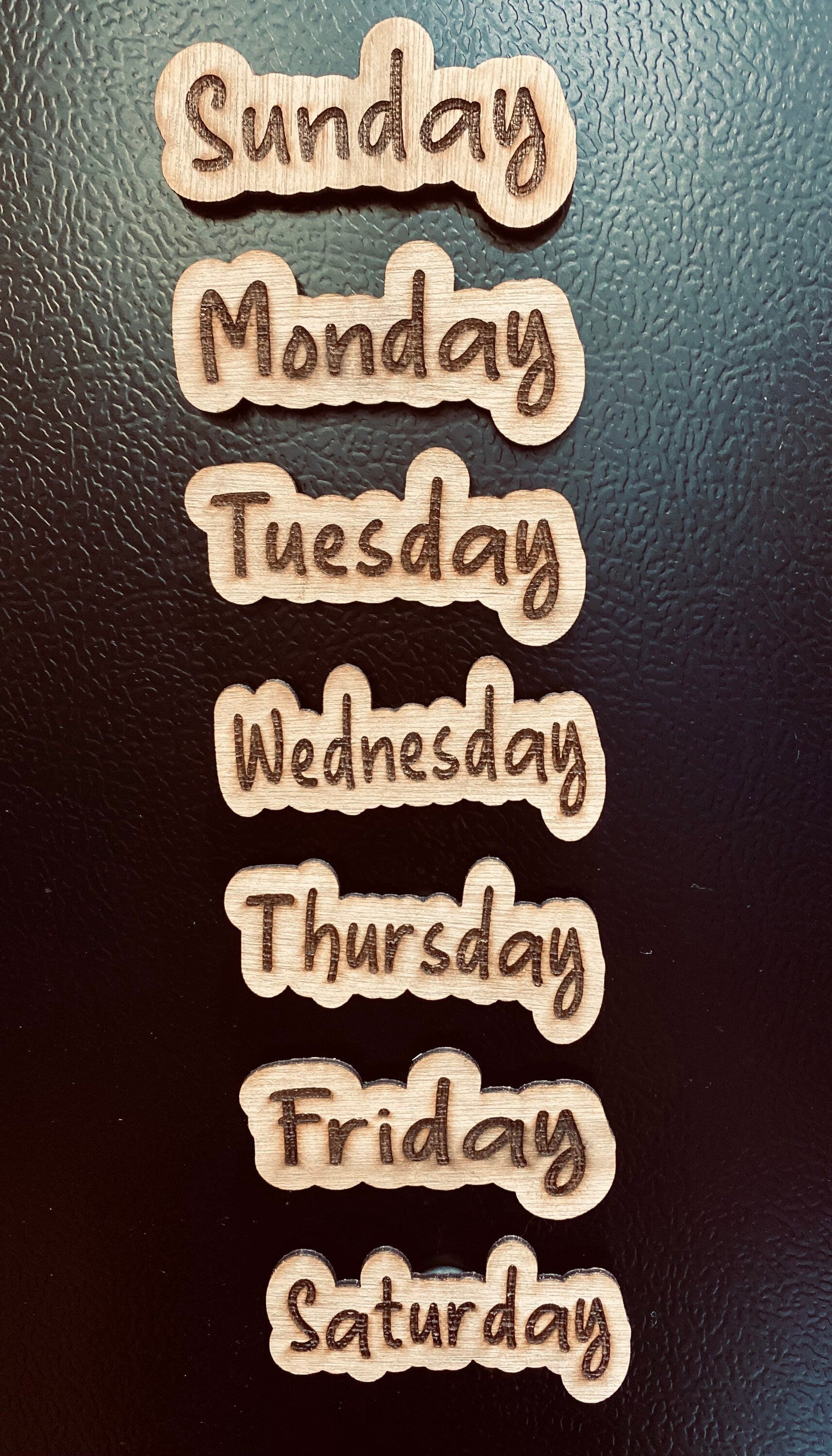 Set of wooden Days of the Week Magnets displayed on a fridge, showcasing their natural finish and laser engraved design.