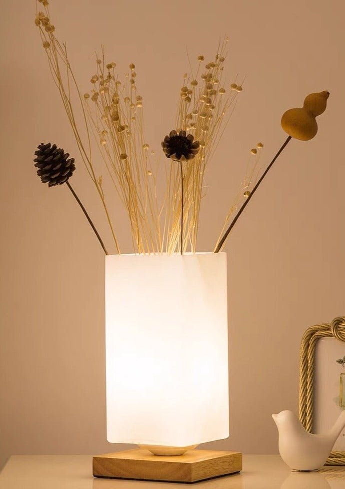 A stylish dimmable flower vase beside a decorative table lamp featuring a frosted glass body and a wooden base, perfect for rustic home decor.