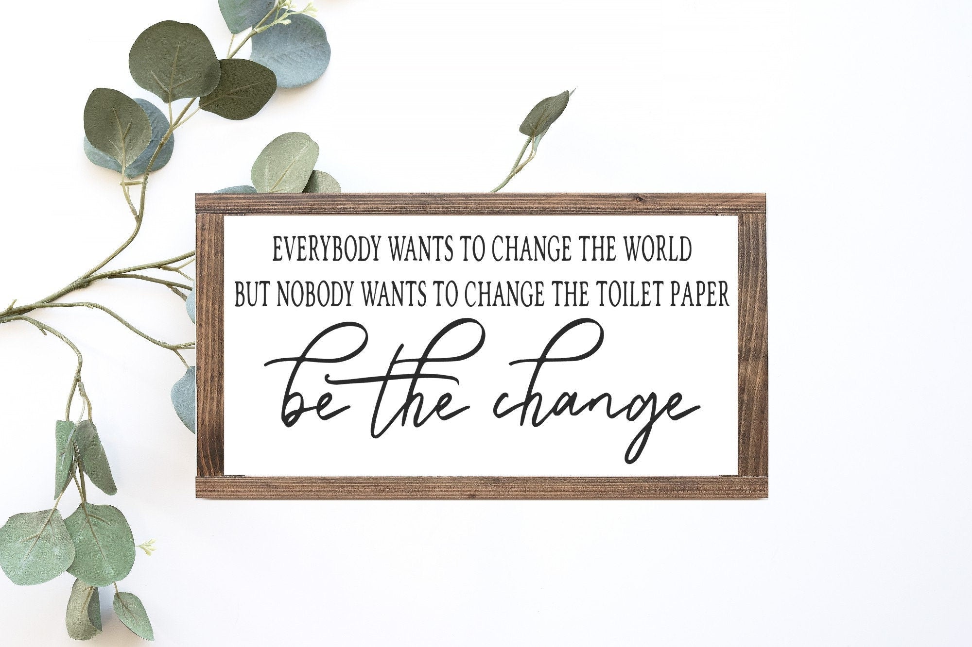 Handmade wooden sign with the phrase 'Be The Change' in matte white finish, showcasing unique wood grain and knots.