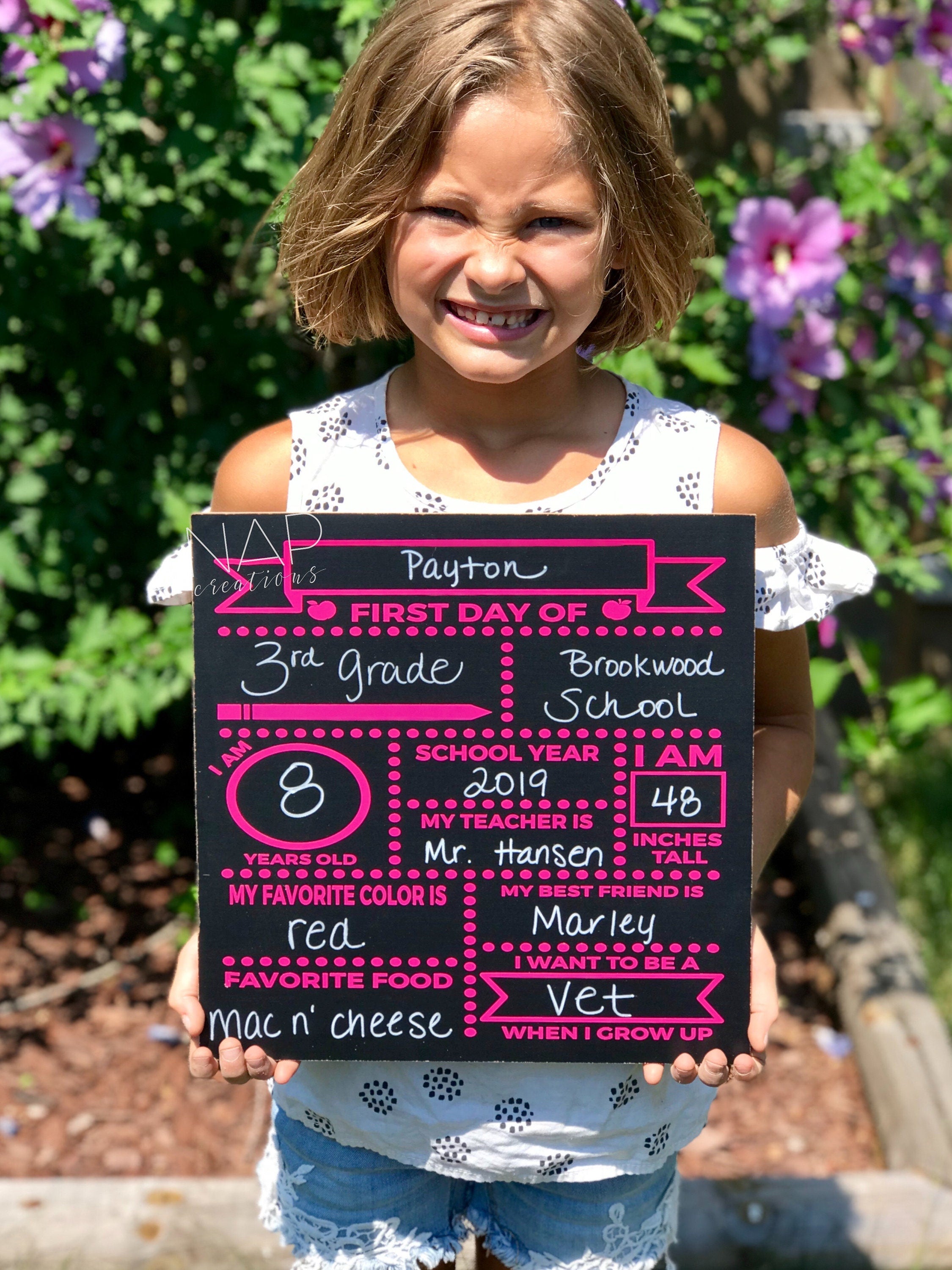 A 12x12 chalkboard designed for first day of school photos, featuring customizable sections for child's name, grade, and favorite things.