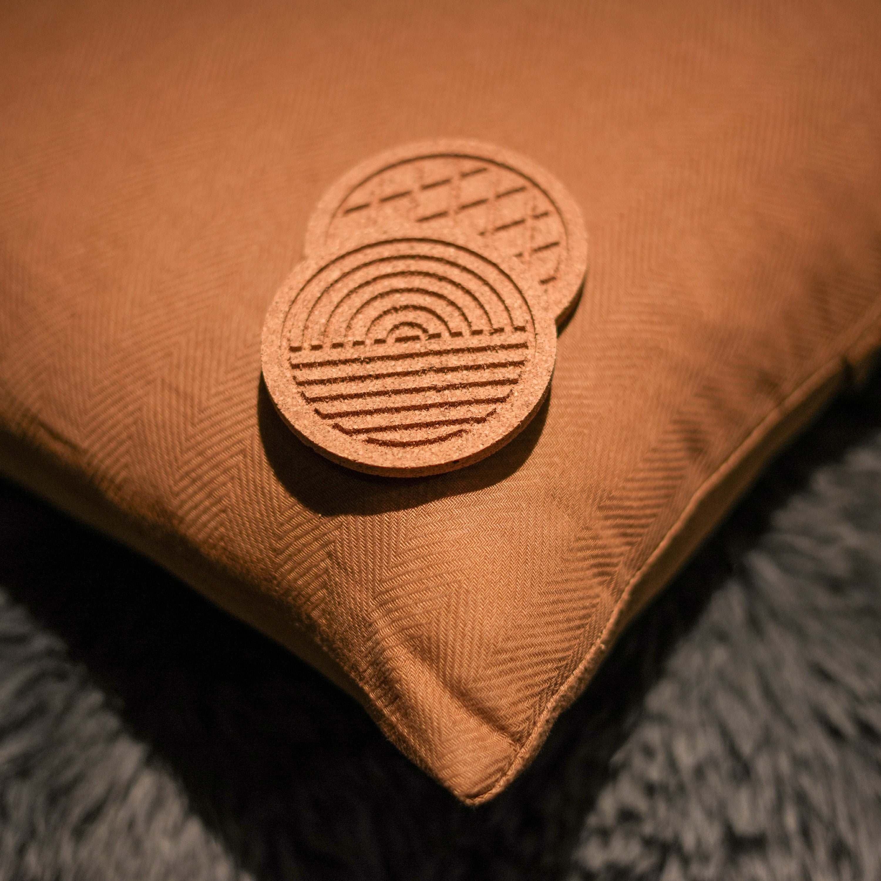 A set of six round cork coasters with nature-inspired designs including waves, leaves, and mountains, elegantly displayed on a wooden table.