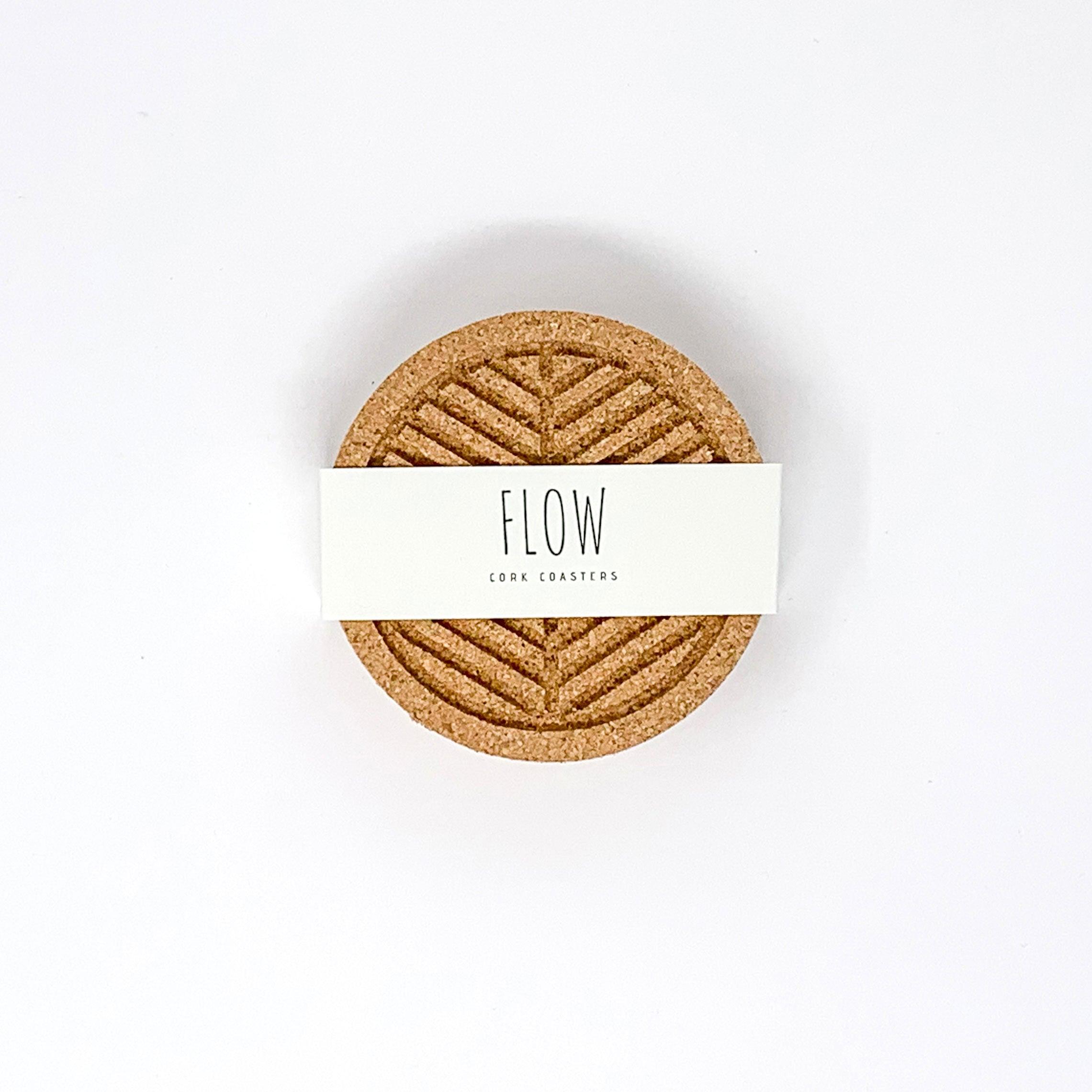 A set of six round cork coasters with nature-inspired designs including waves, leaves, and mountains, elegantly displayed on a wooden table.