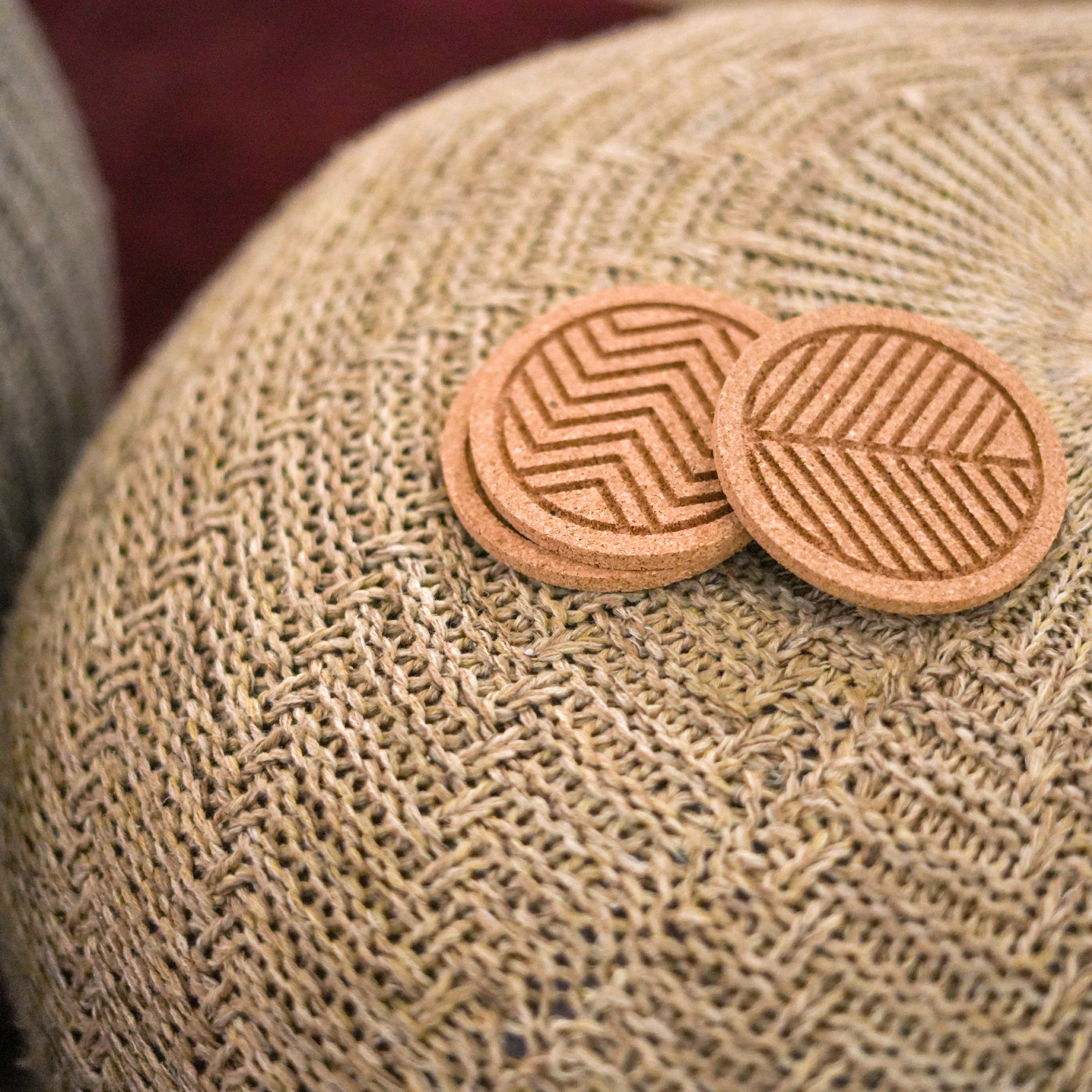 A set of six round cork coasters with nature-inspired designs including waves, leaves, and mountains, elegantly displayed on a wooden table.