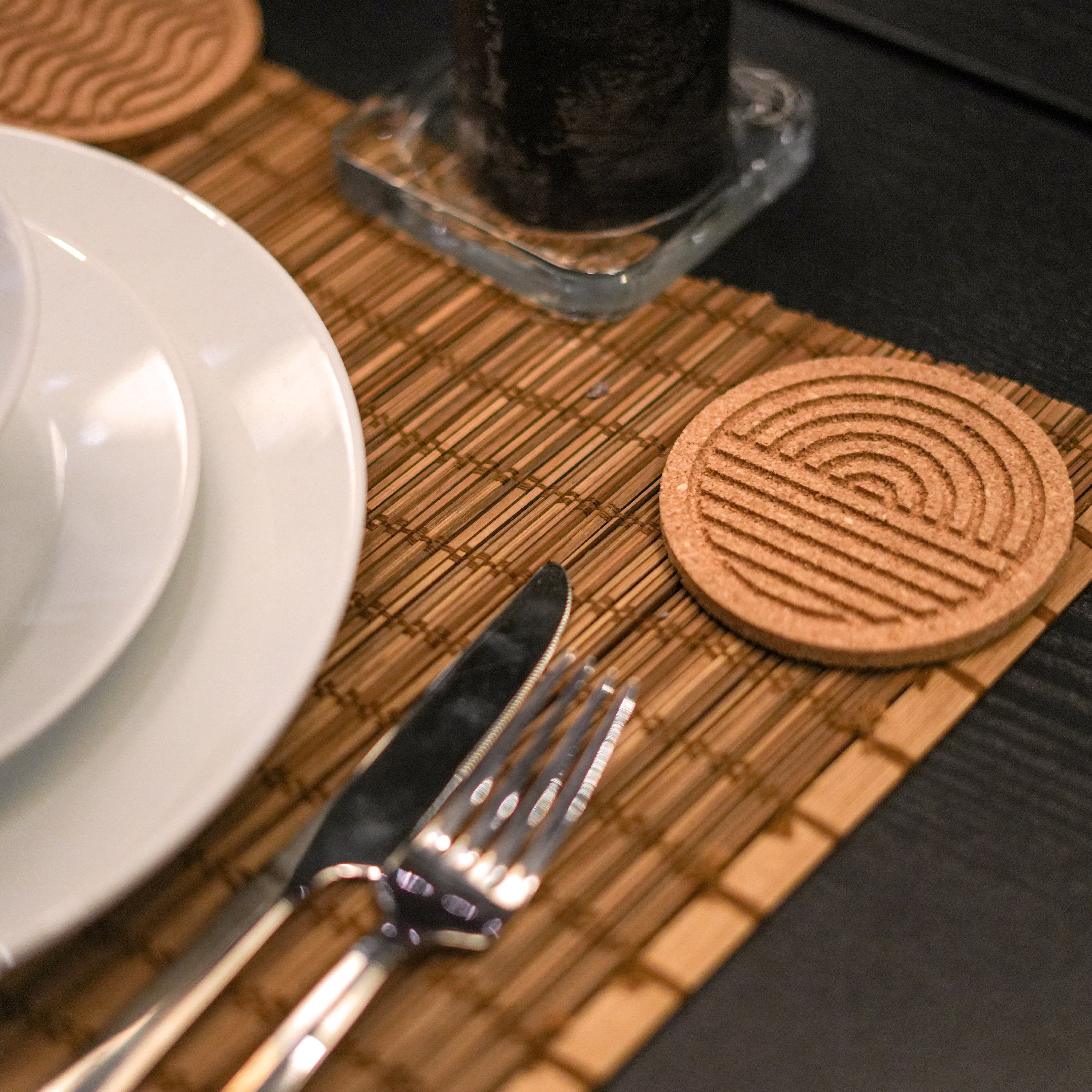 A set of six round cork coasters with nature-inspired designs including waves, leaves, and mountains, elegantly displayed on a wooden table.