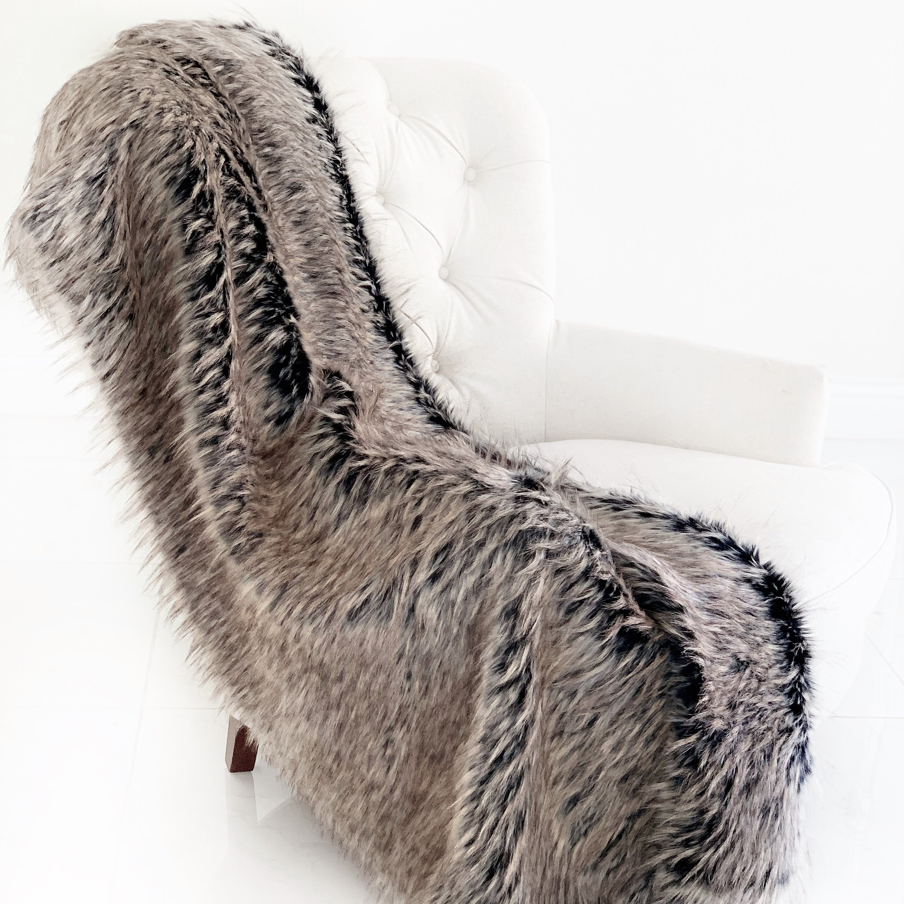 Foxy Brown Gray Plush Handmade Luxury Faux Fur Throw blanket draped elegantly on a couch, showcasing its soft texture and reversible design.