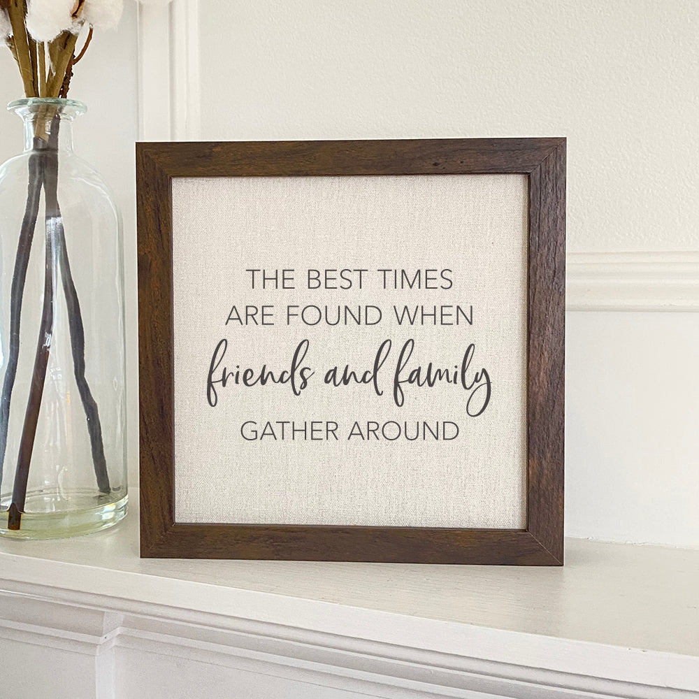 A beautifully framed sign that reads 'Friends Family Gather Around', featuring a natural wood frame and a linen-look background.