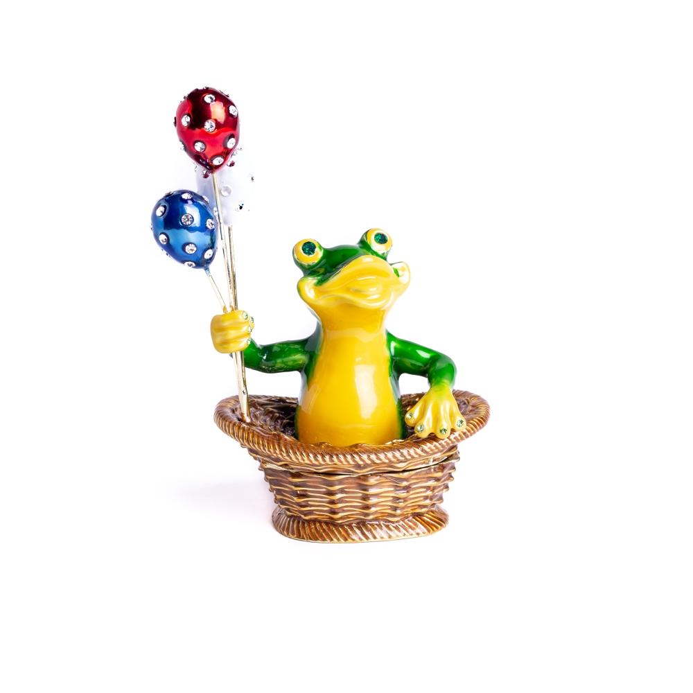 A handmade trinket box featuring a frog sitting in a basket, holding colorful balloons, adorned with Austrian crystals and plated with 925 silver.