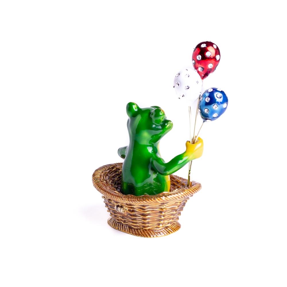 A handmade trinket box featuring a frog sitting in a basket, holding colorful balloons, adorned with Austrian crystals and plated with 925 silver.