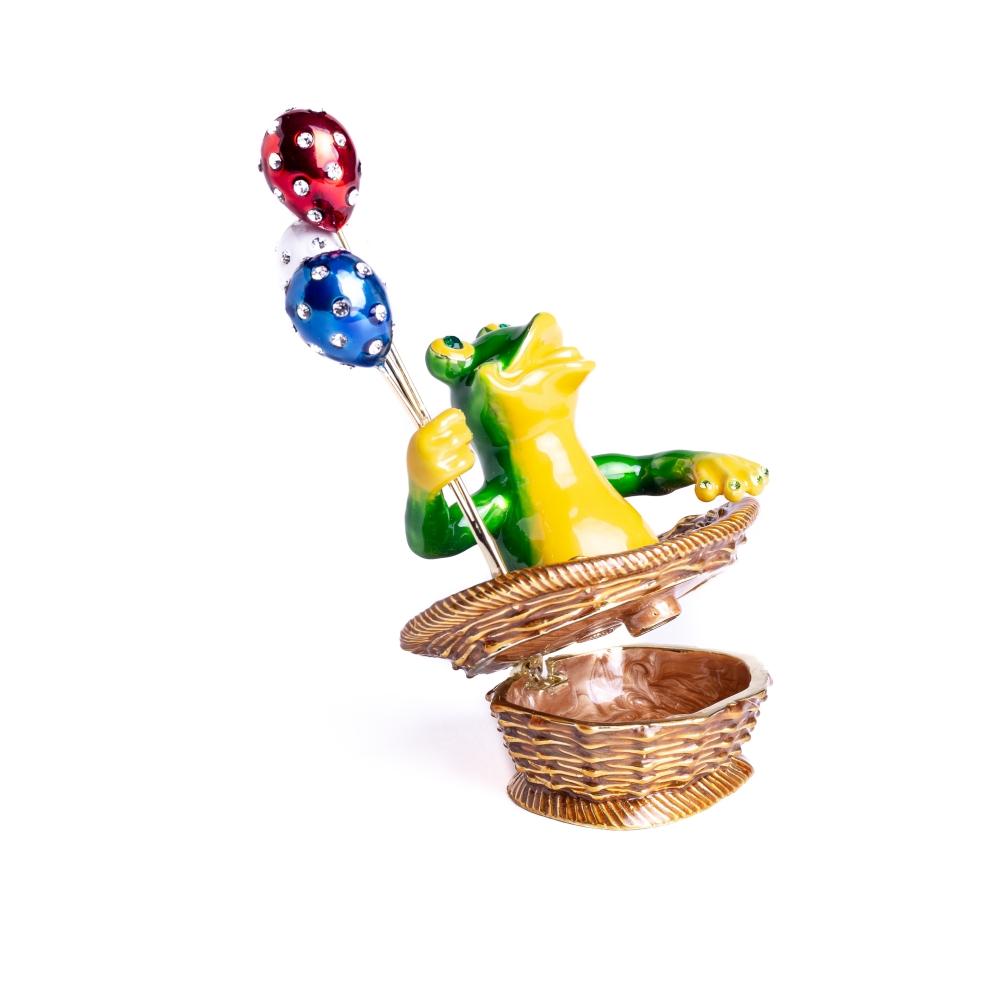 A handmade trinket box featuring a frog sitting in a basket, holding colorful balloons, adorned with Austrian crystals and plated with 925 silver.