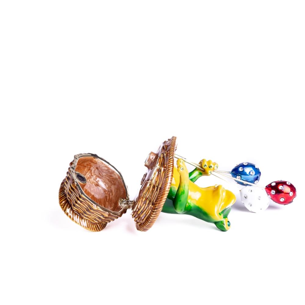 A handmade trinket box featuring a frog sitting in a basket, holding colorful balloons, adorned with Austrian crystals and plated with 925 silver.